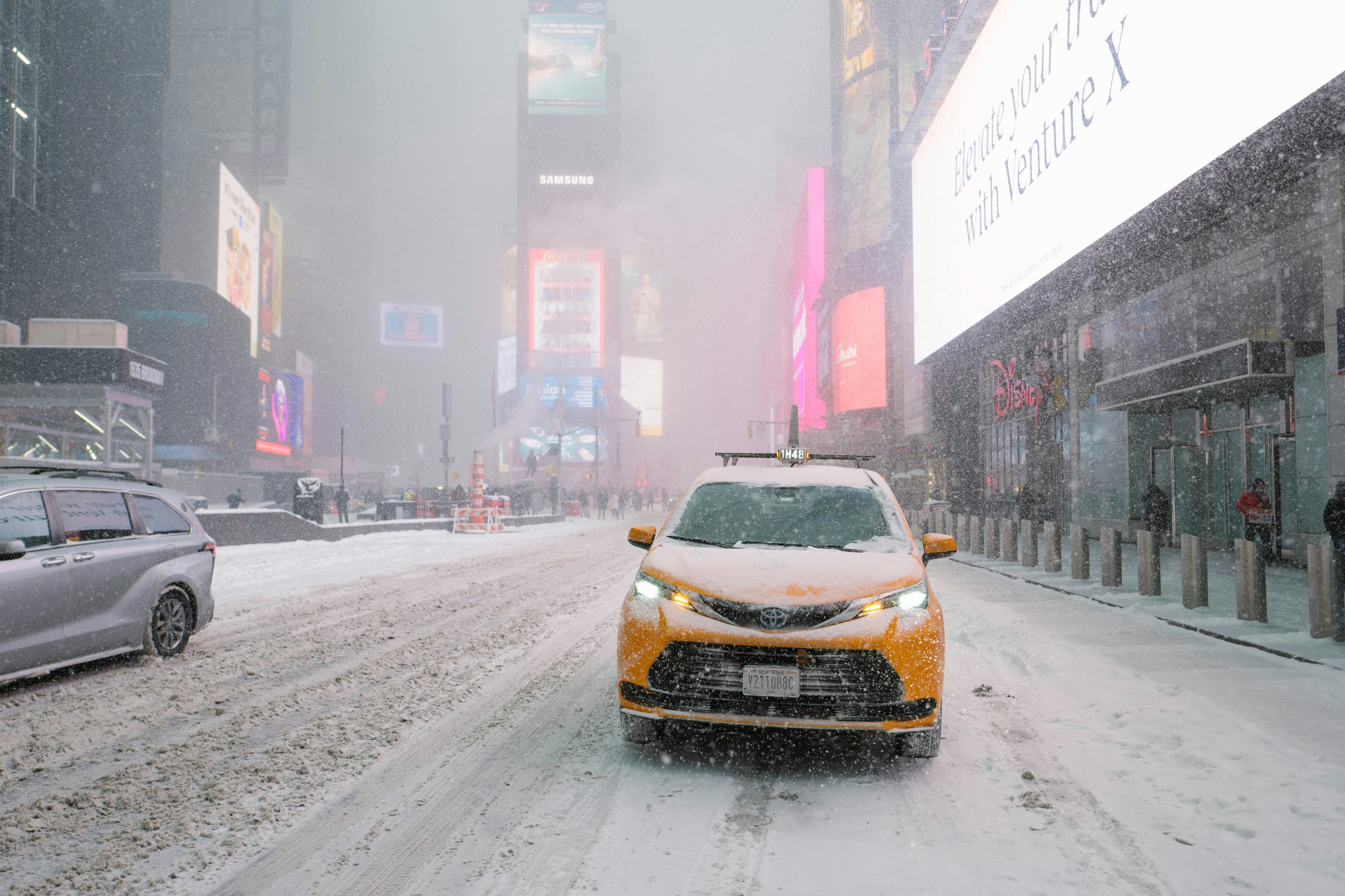 Yellow taxi drives through snowy times square