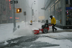 Man clearing snow with a snowblower on a city street.