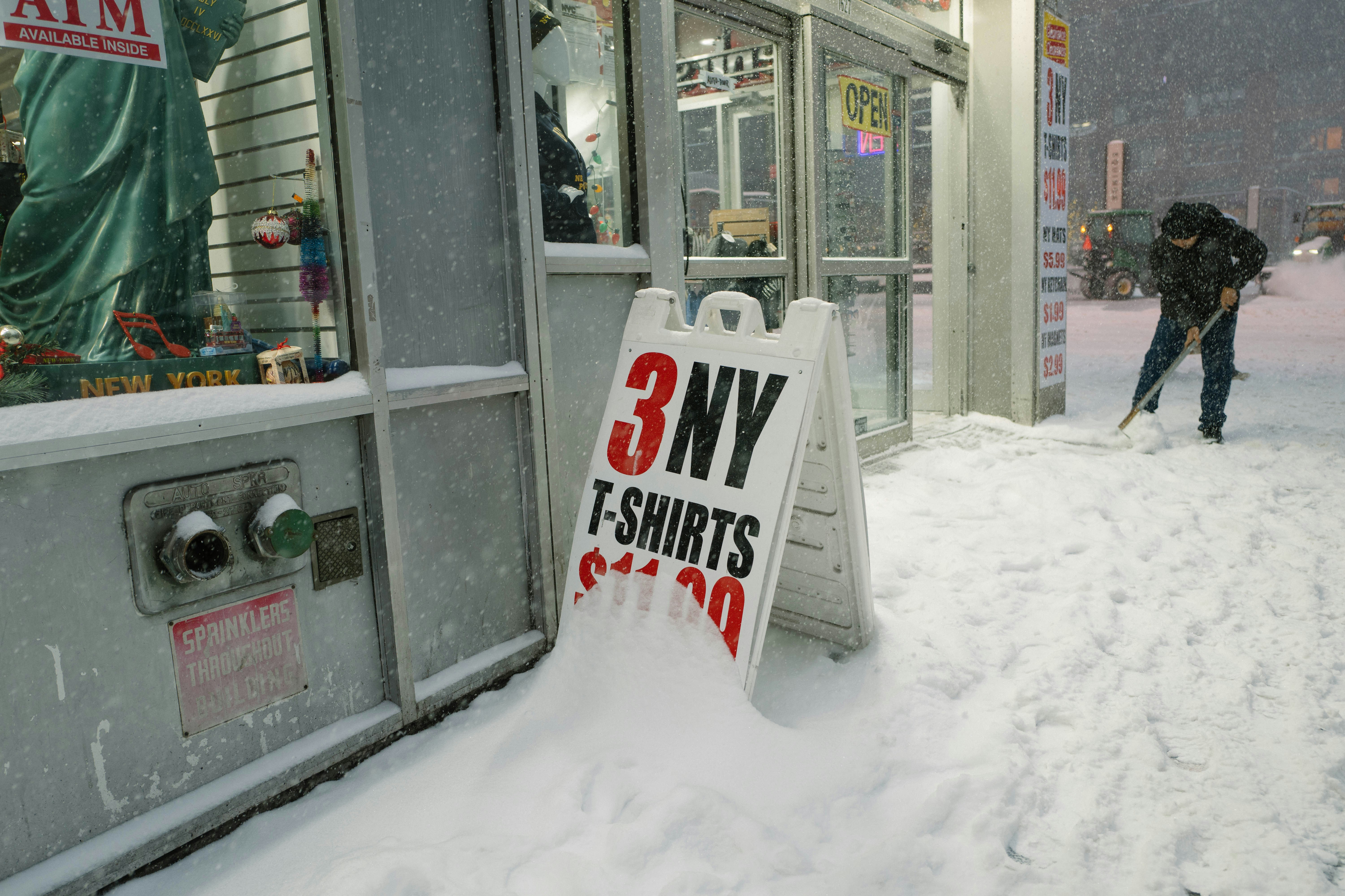 Man shoveling snow in front of store during a snowstorm.