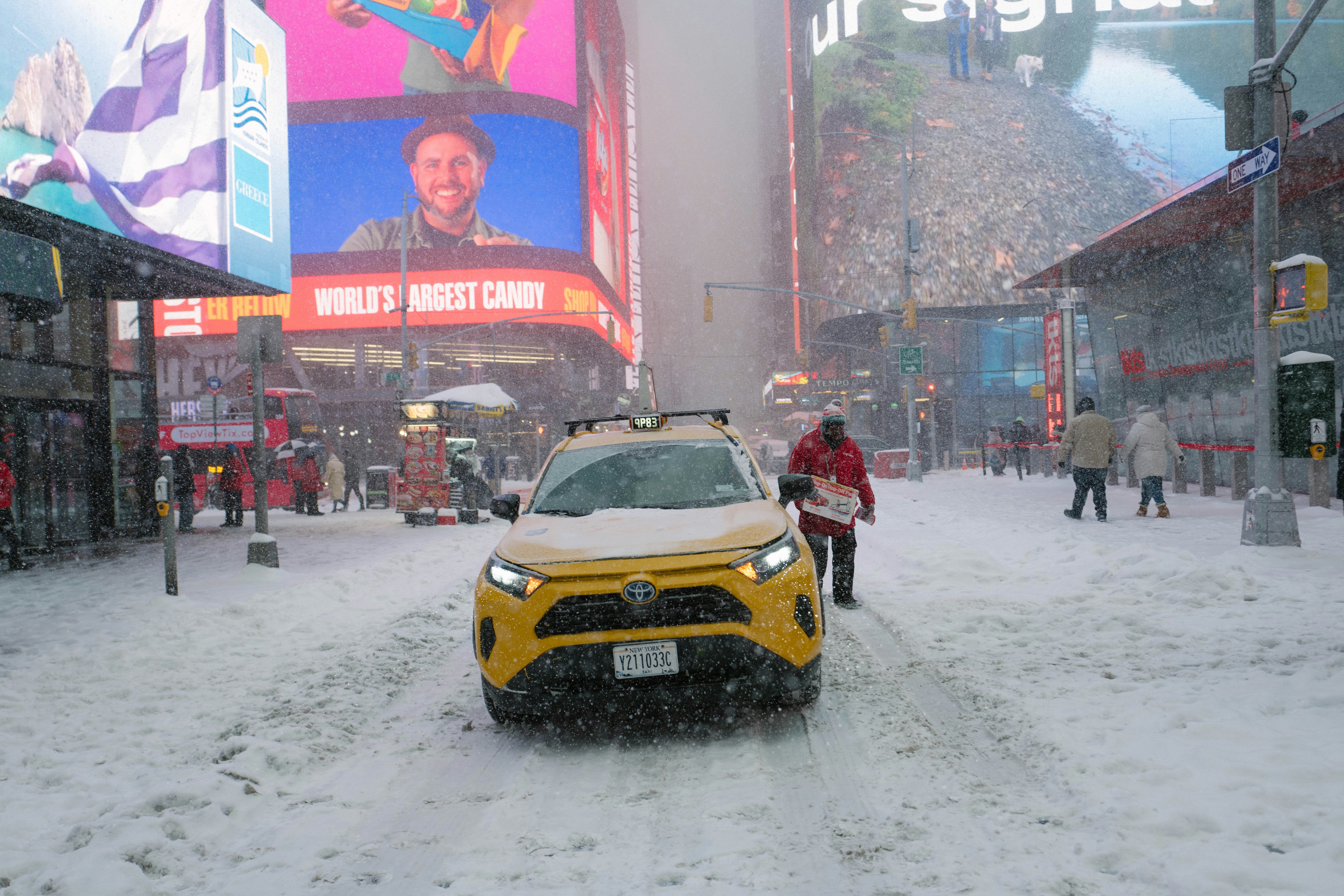 Yellow taxi driving through snowy times square.