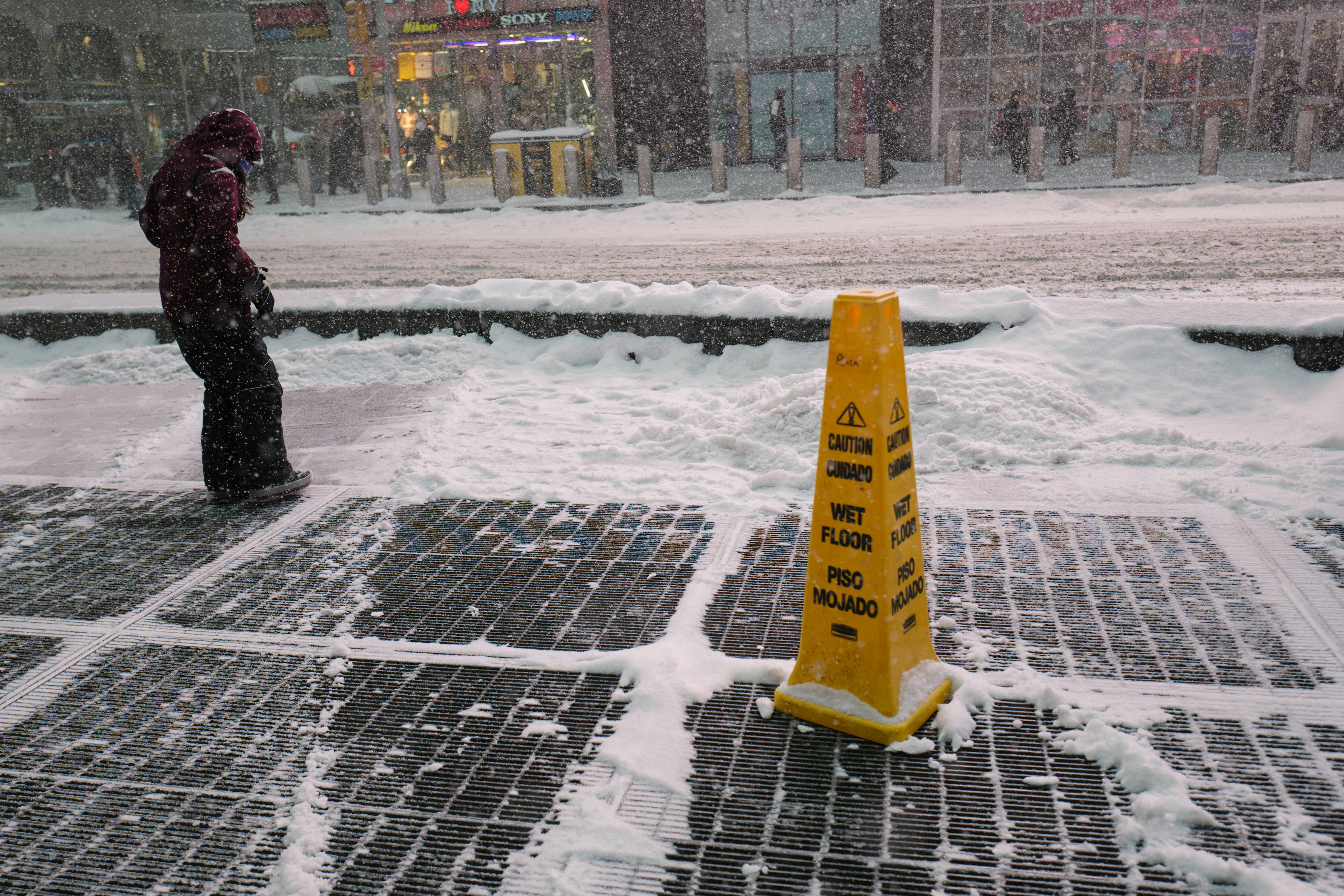 A person walks past a wet floor sign in snow.