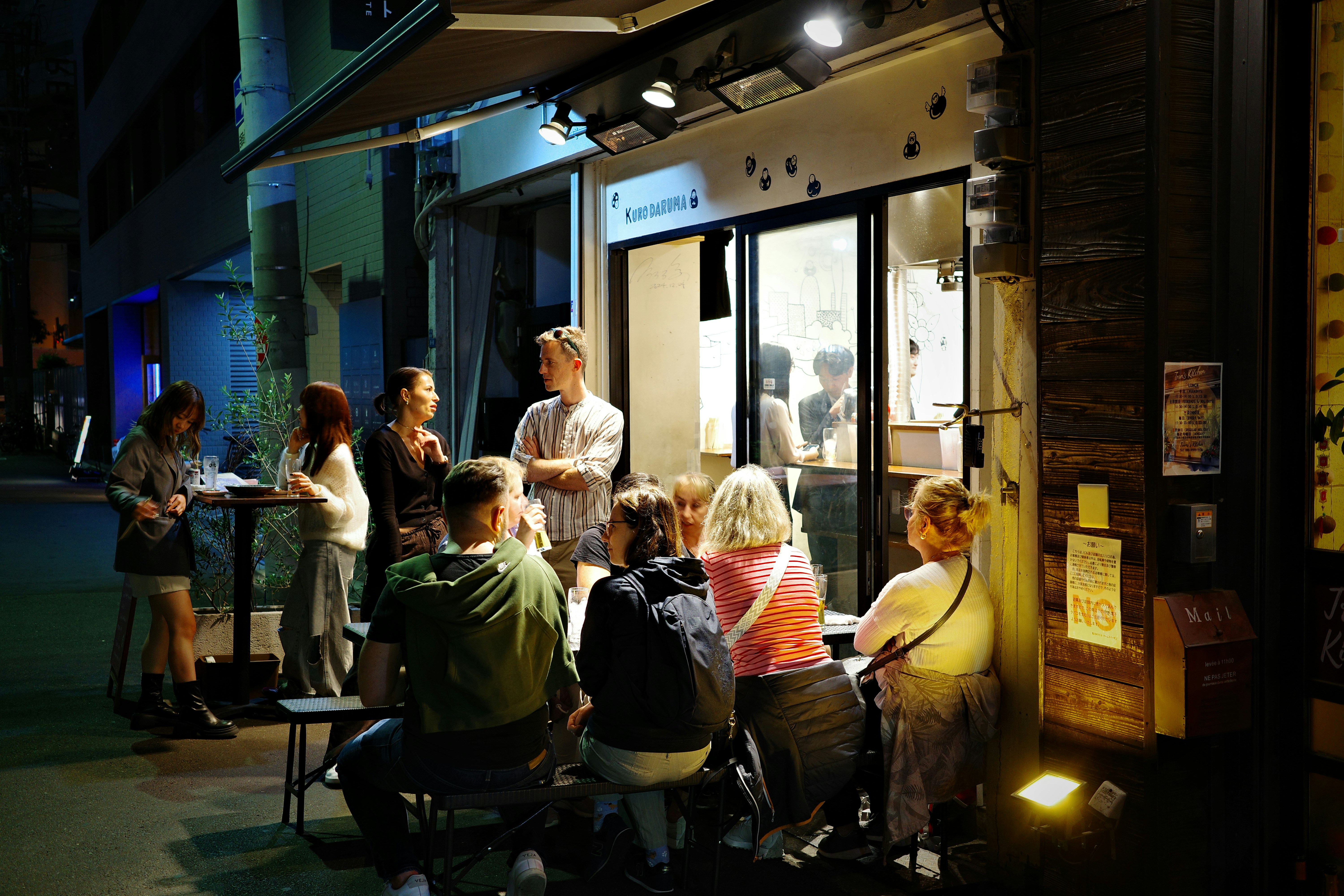 People gathered outside a brightly lit restaurant at night.