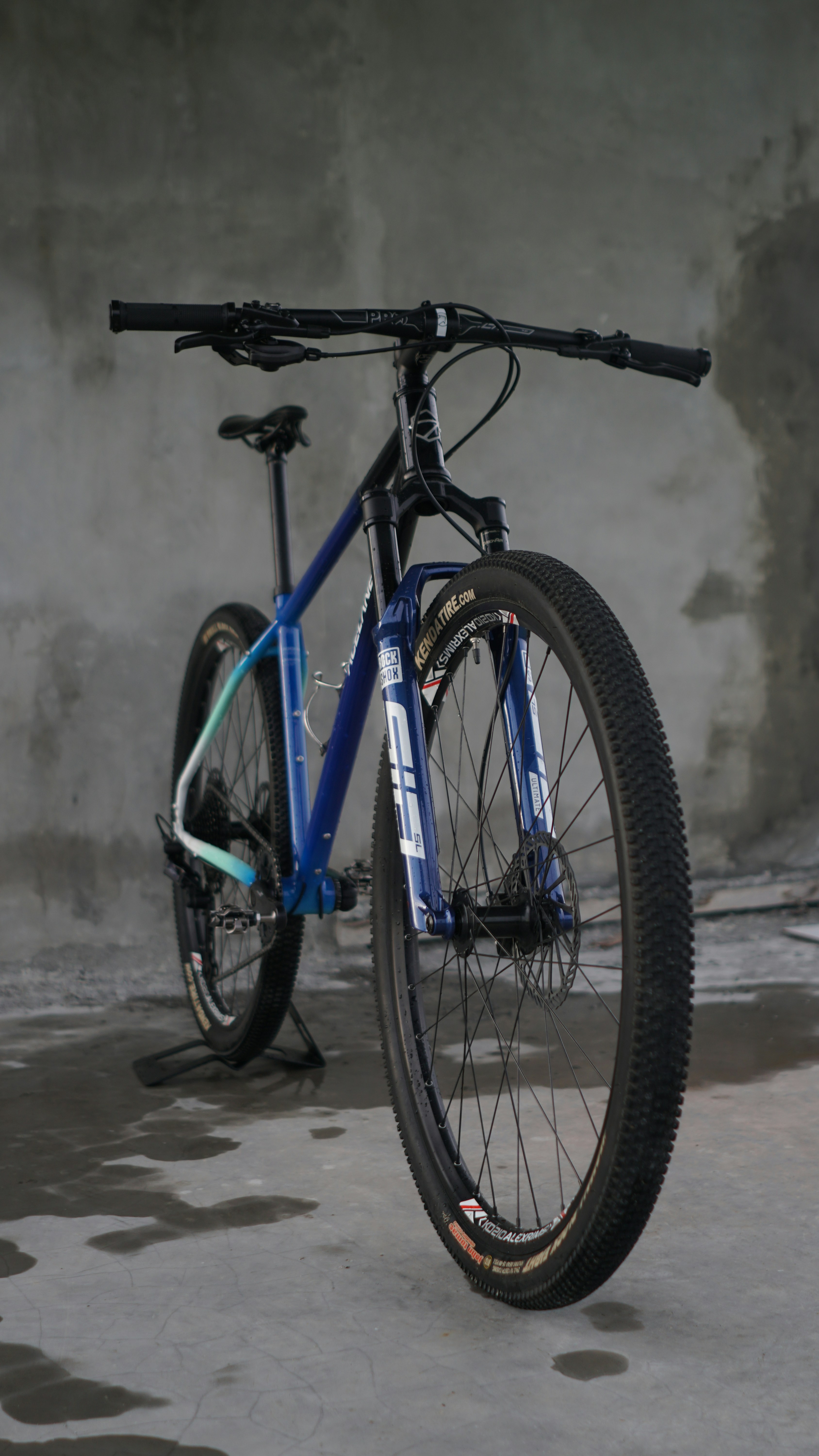 A blue mountain bike stands on a concrete floor.