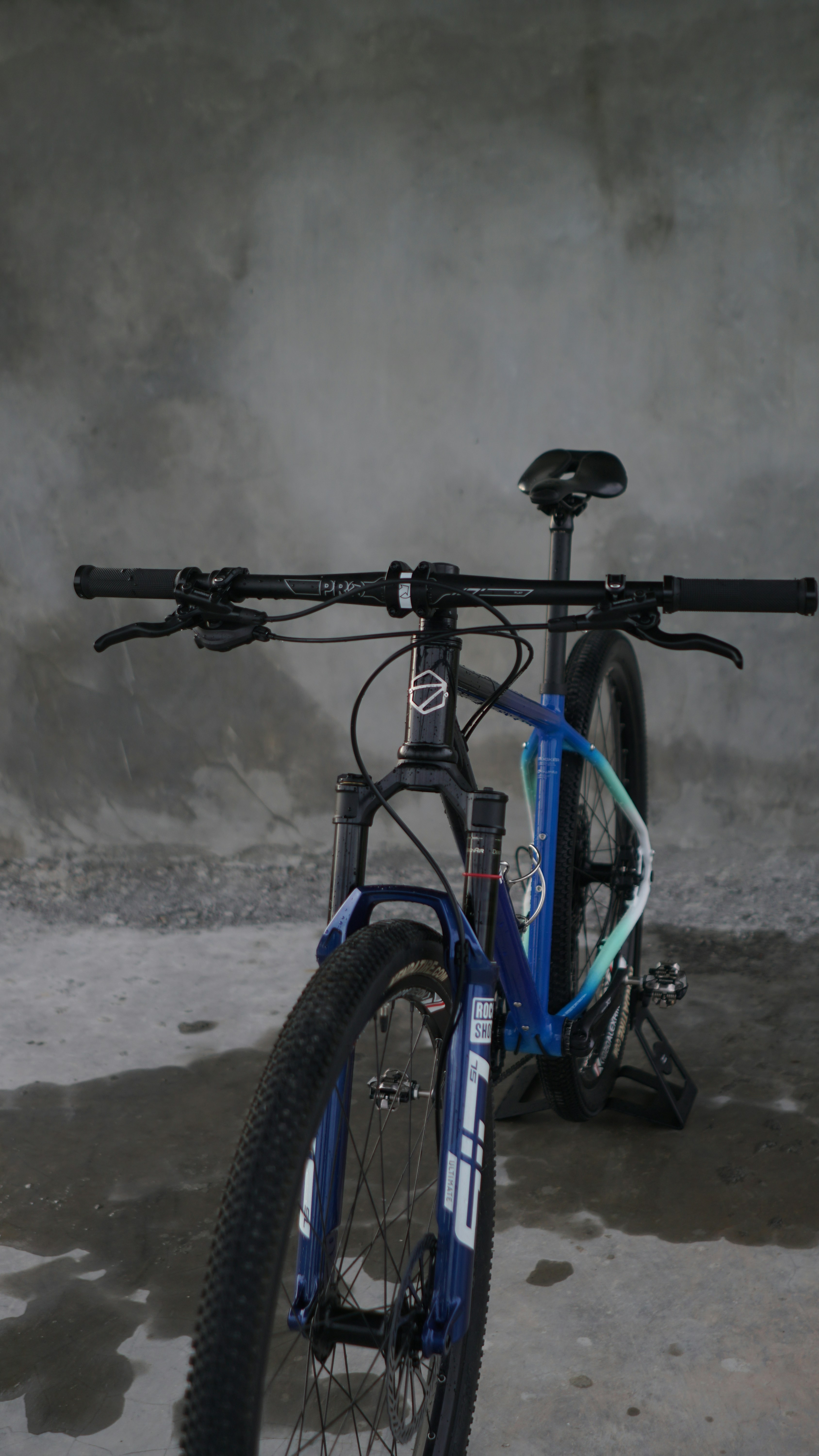 A blue mountain bike parked against a concrete wall.