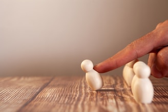 Finger pushing a small wooden figure over a group.