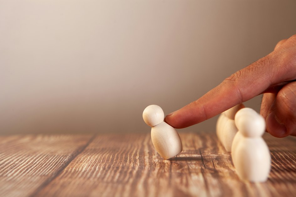 A finger pushing a small wooden figure over a group of wooden figures