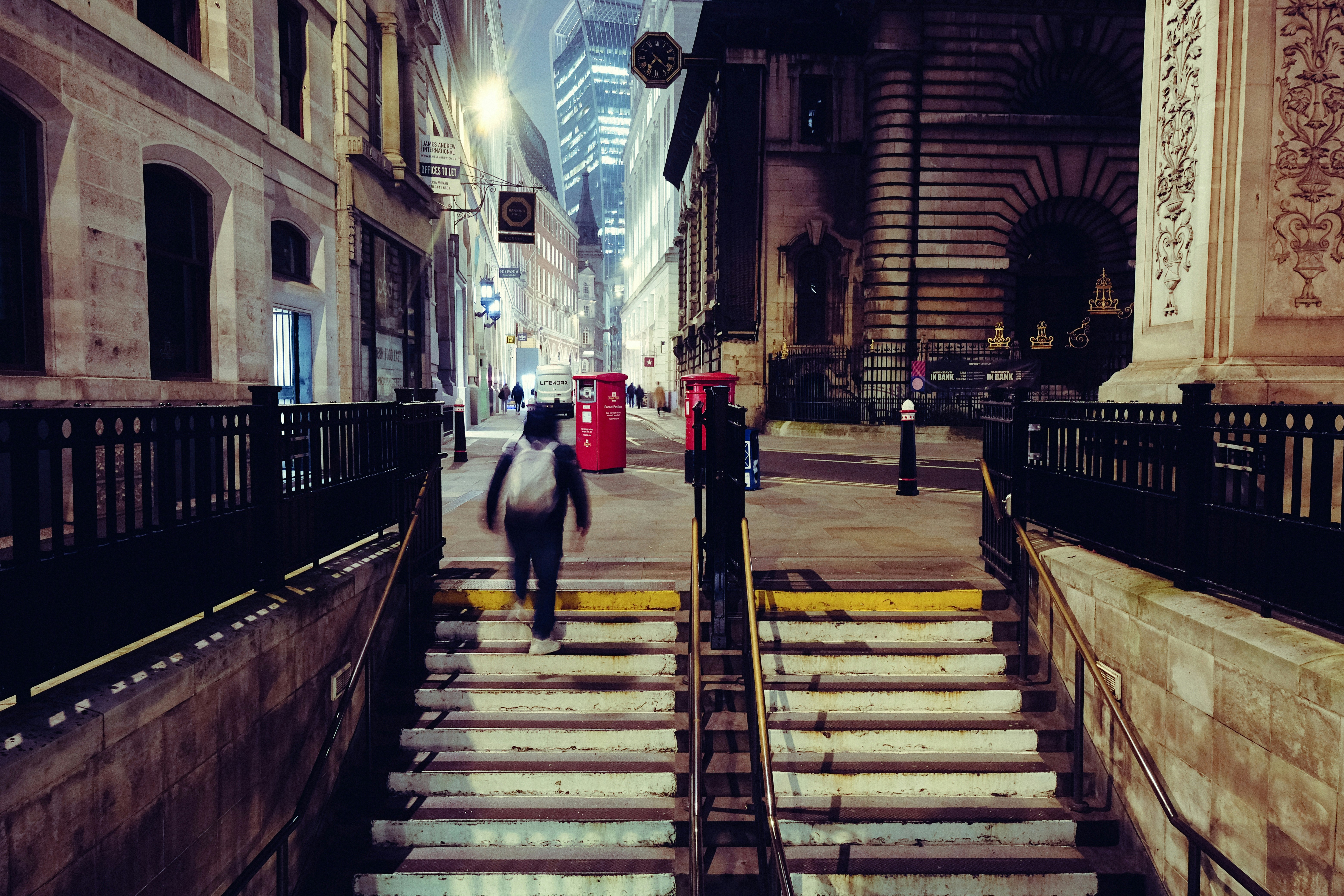 Person walks up stairs on a city street at night.