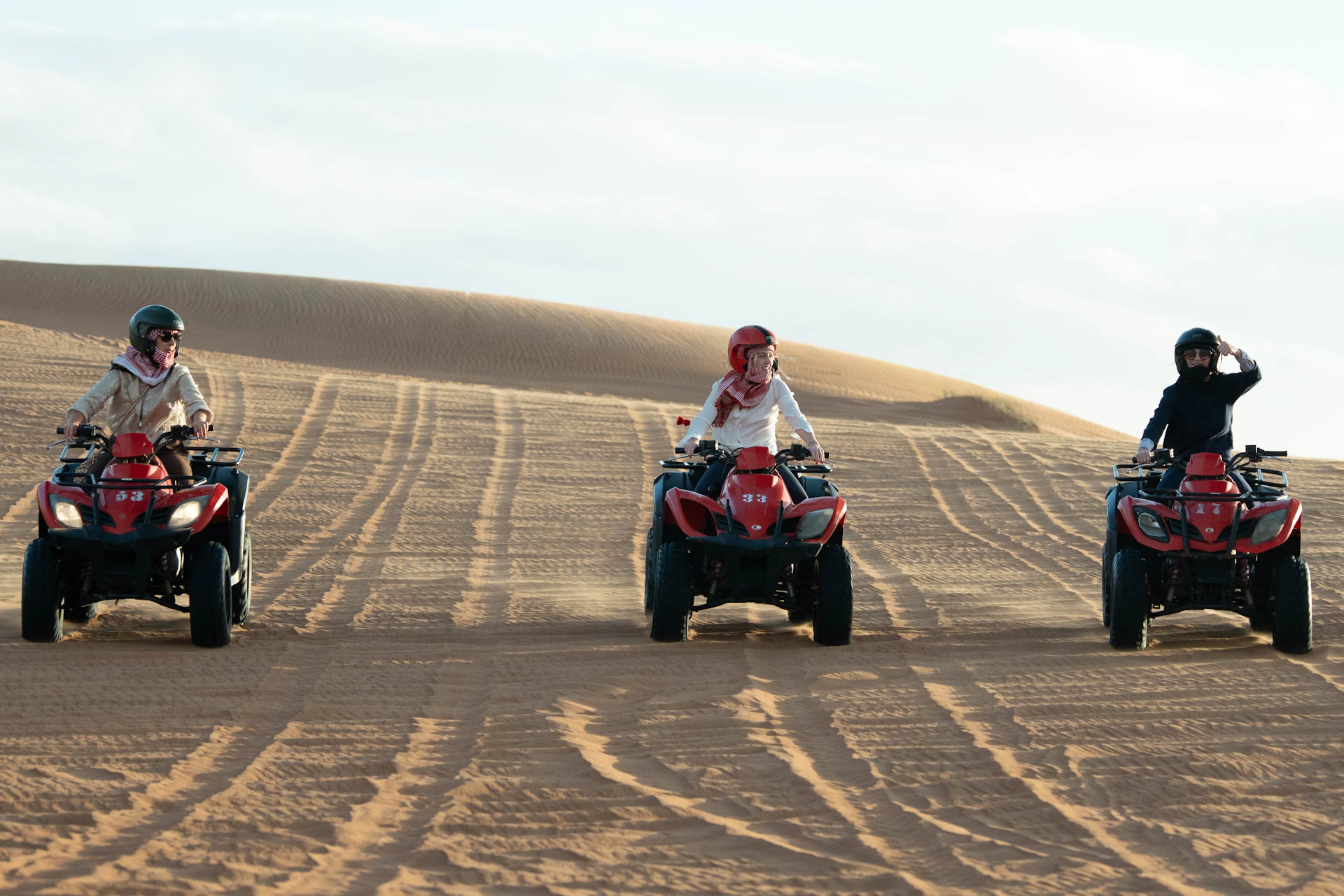 Three people riding atvs on sand dunes