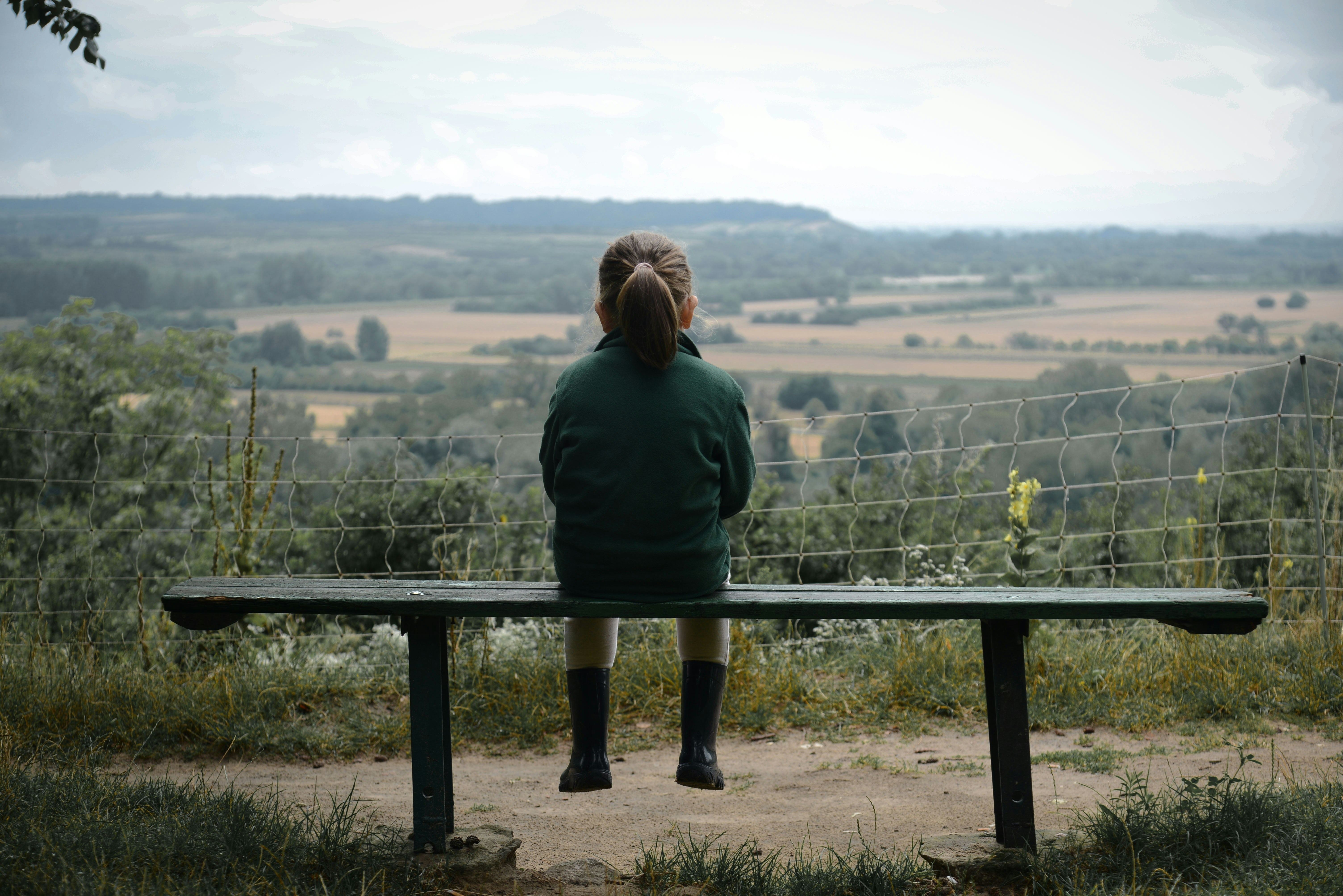 A young girl sits on a bench overlooking a valley.
