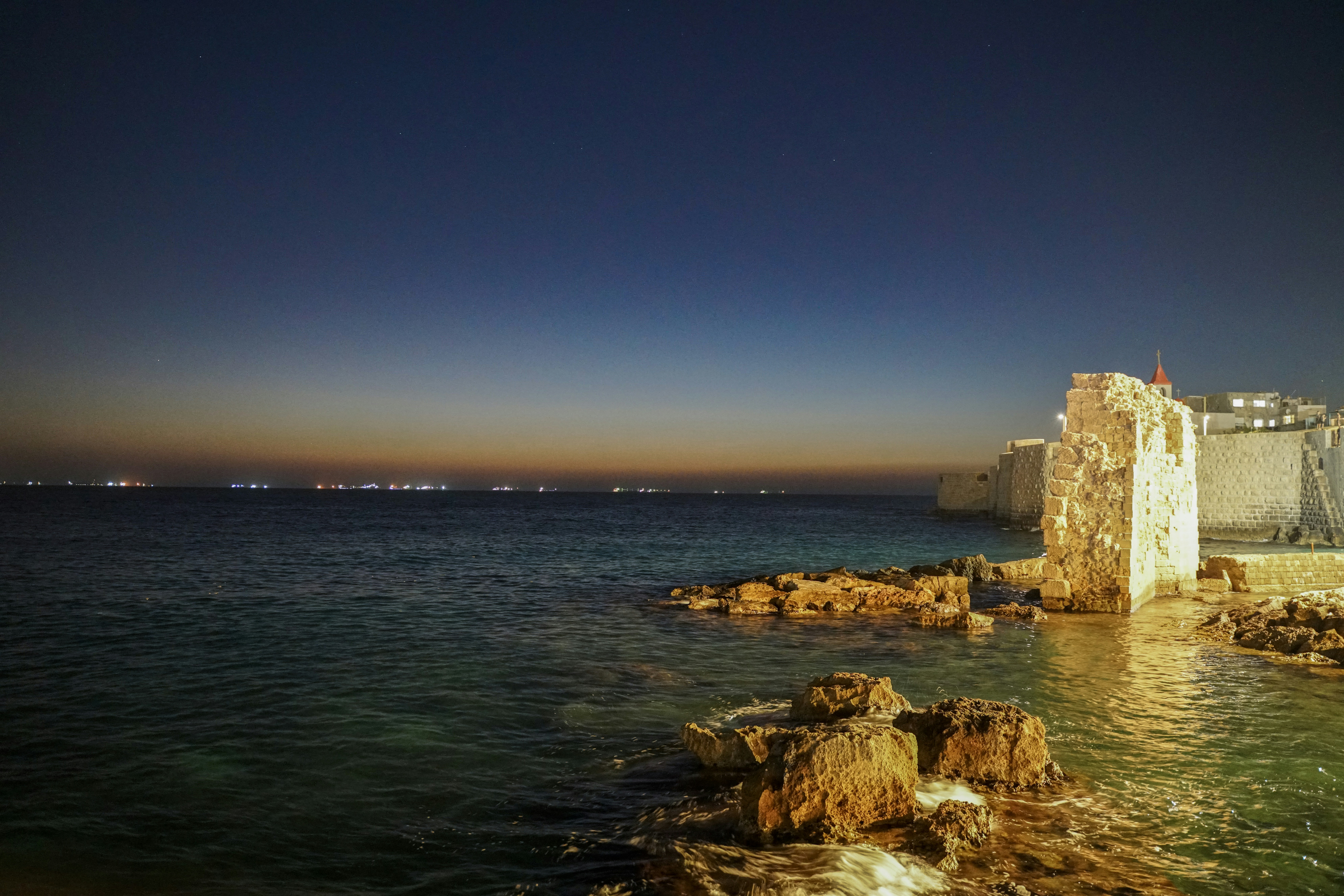 Coastal town with ancient stone structure at dusk.
