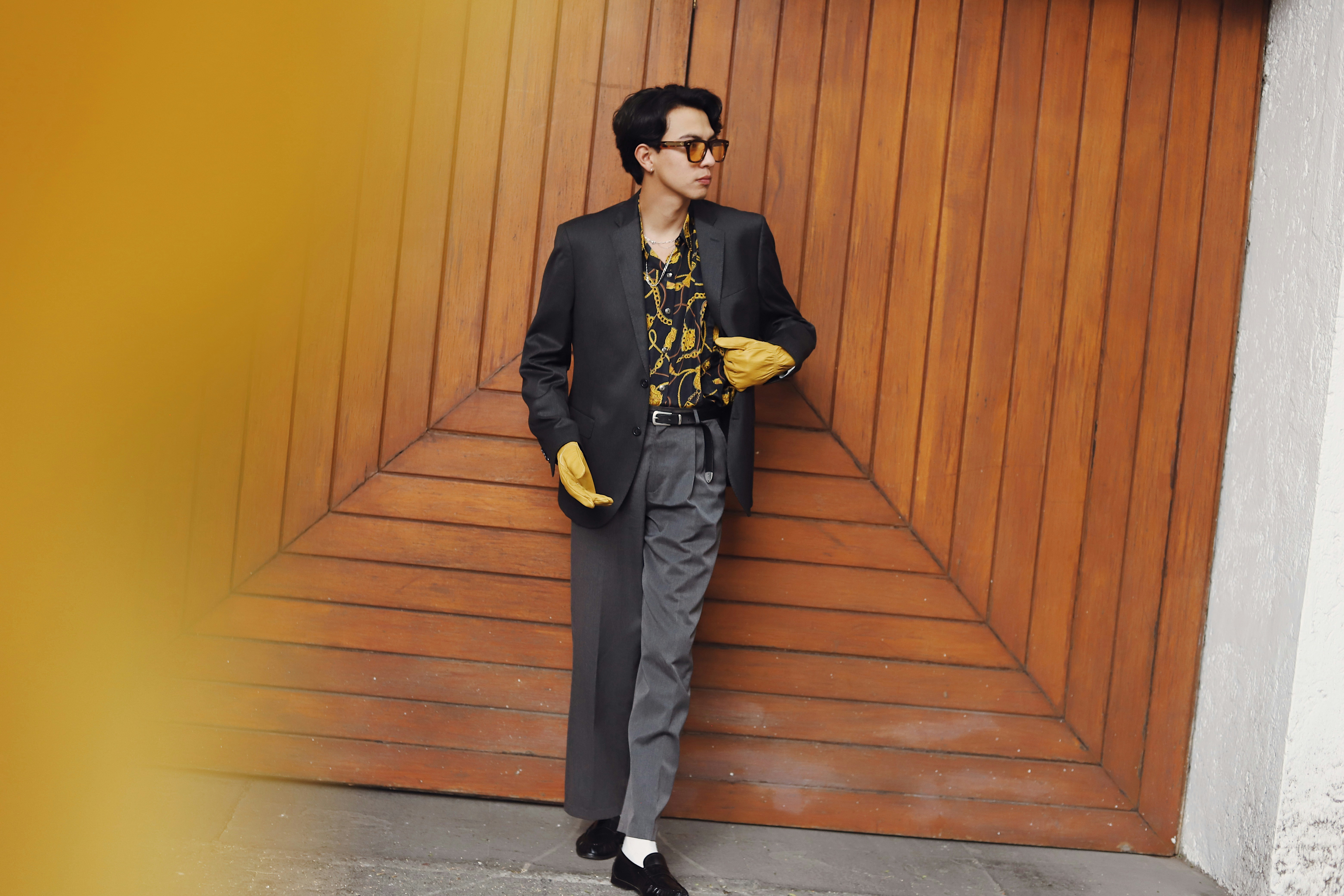 Man in stylish suit and gloves stands by wooden door.