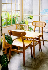 Wooden chairs and table near a window with plants.