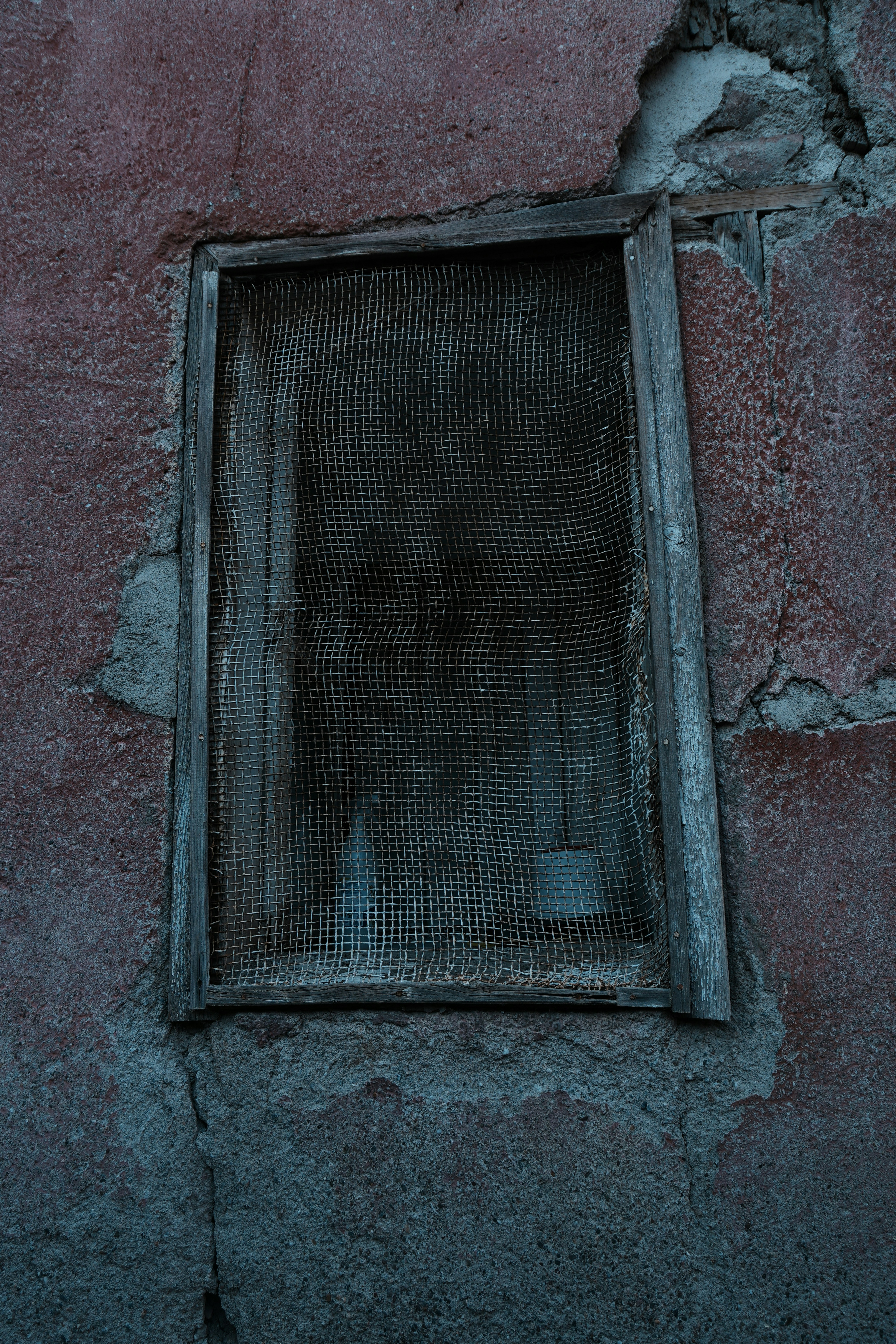 Ein altes, verwittertes Fenster mit beschädigtem Fliegengitter.