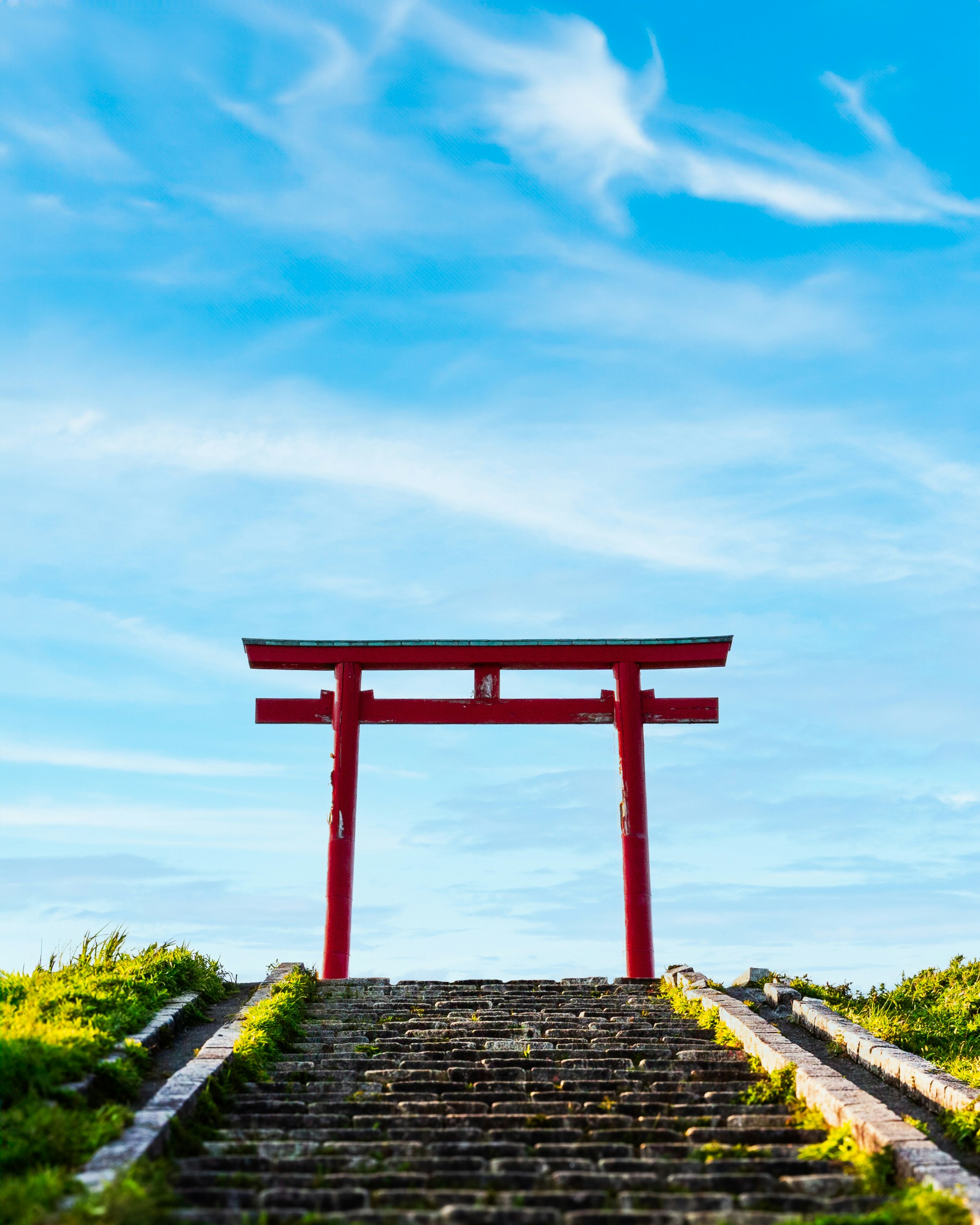 Porta torii rossa su scale di pietra sotto un cielo azzurro