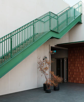 A green staircase ascends a white wall beside potted plants.