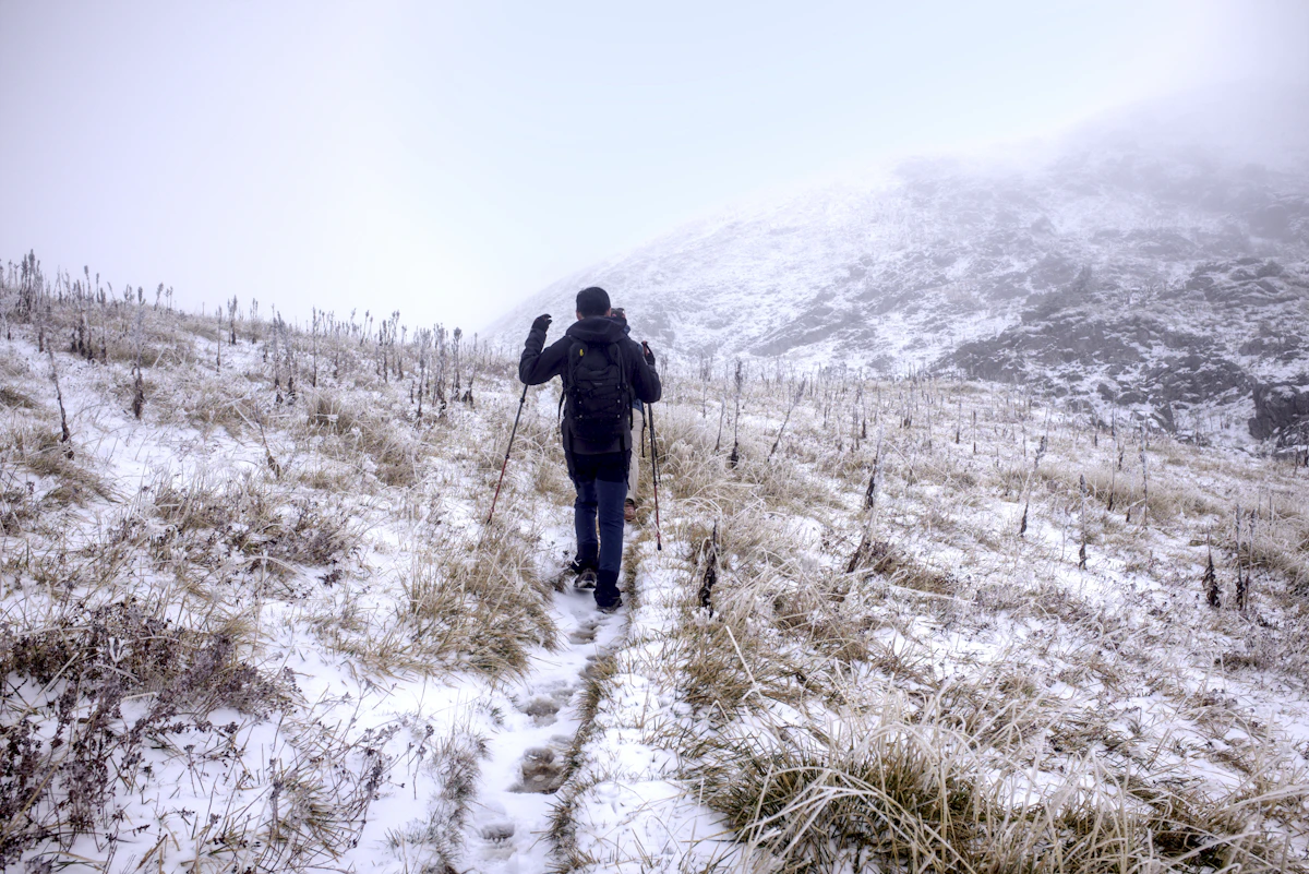 Hiker climbing snowy trail with aluminum trekking poles