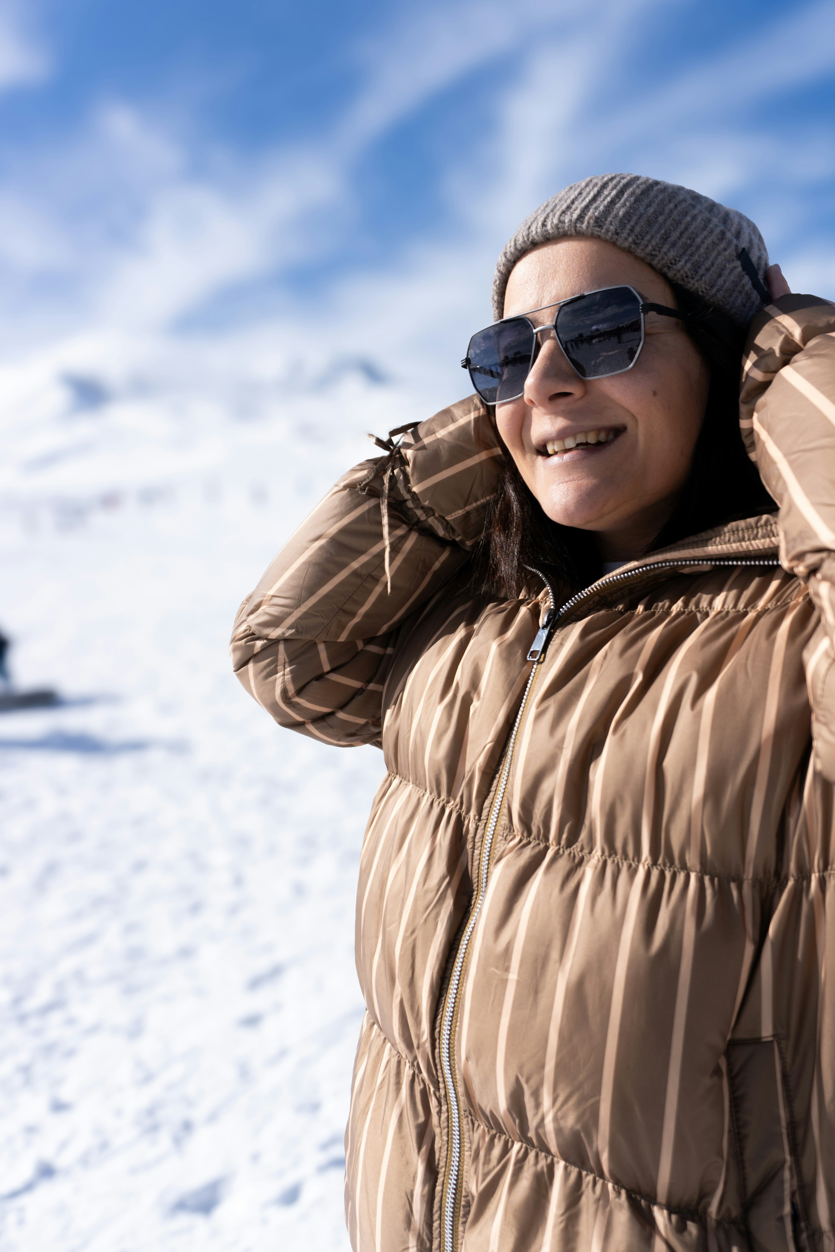 Young woman in winter clothing and sunglasses smiles.