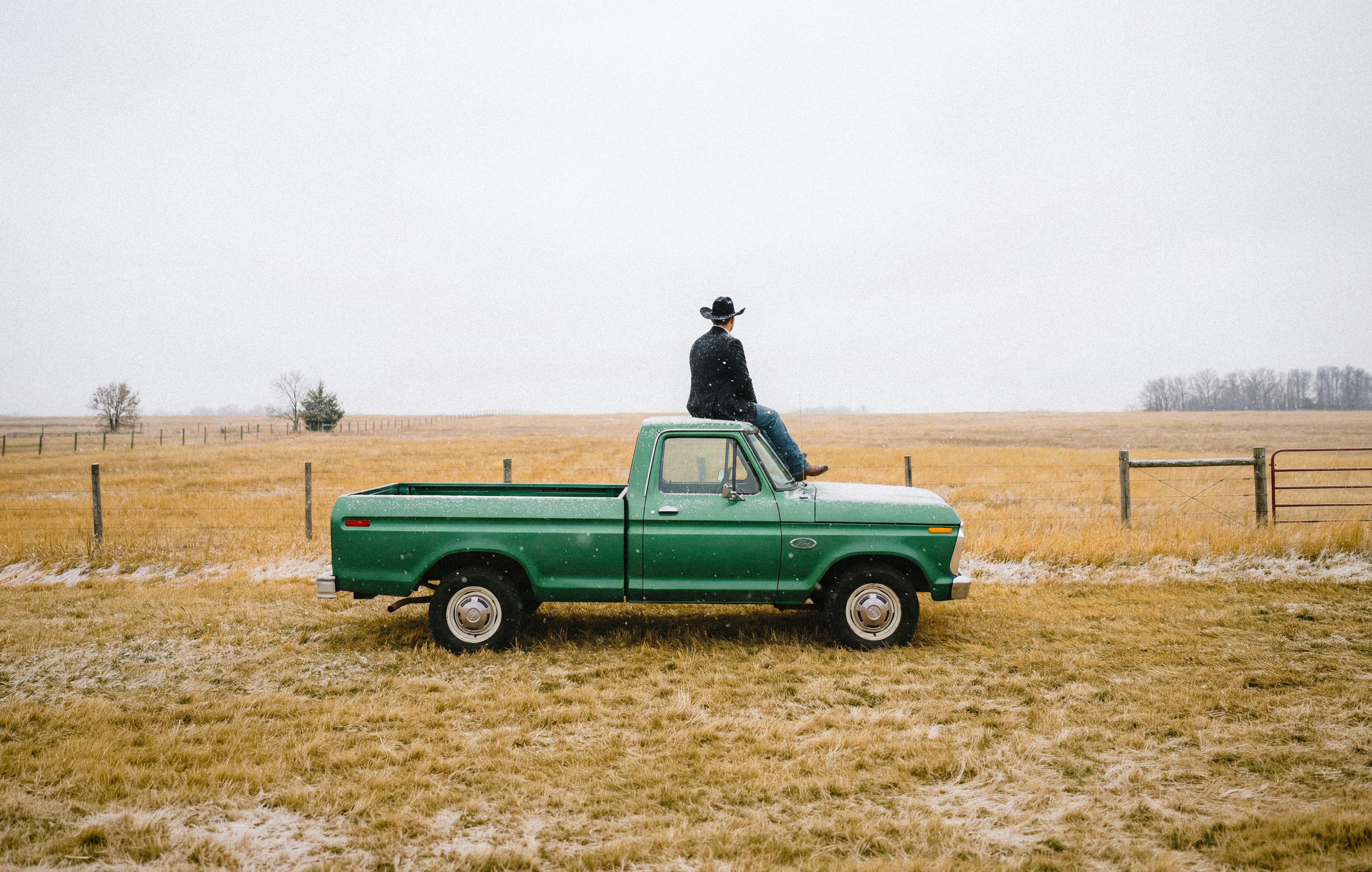 Person sitting on green pickup truck in a field