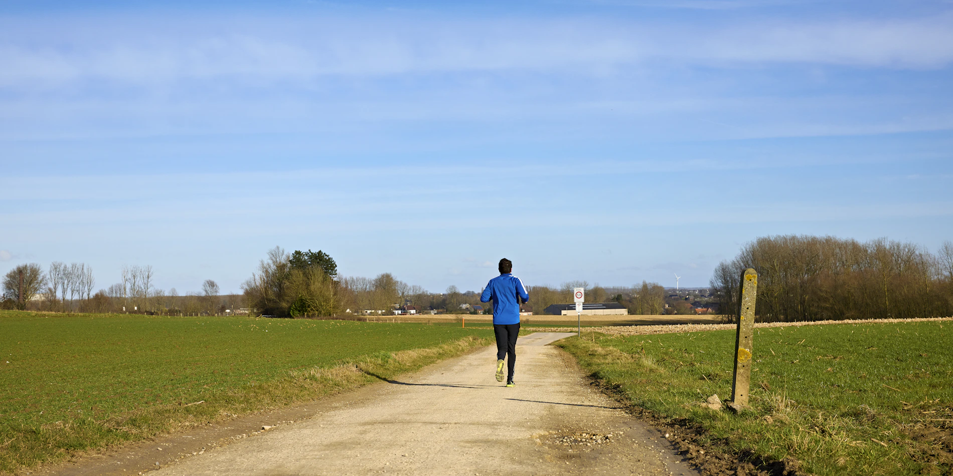 Runner moving along a rural dirt path through open green fields