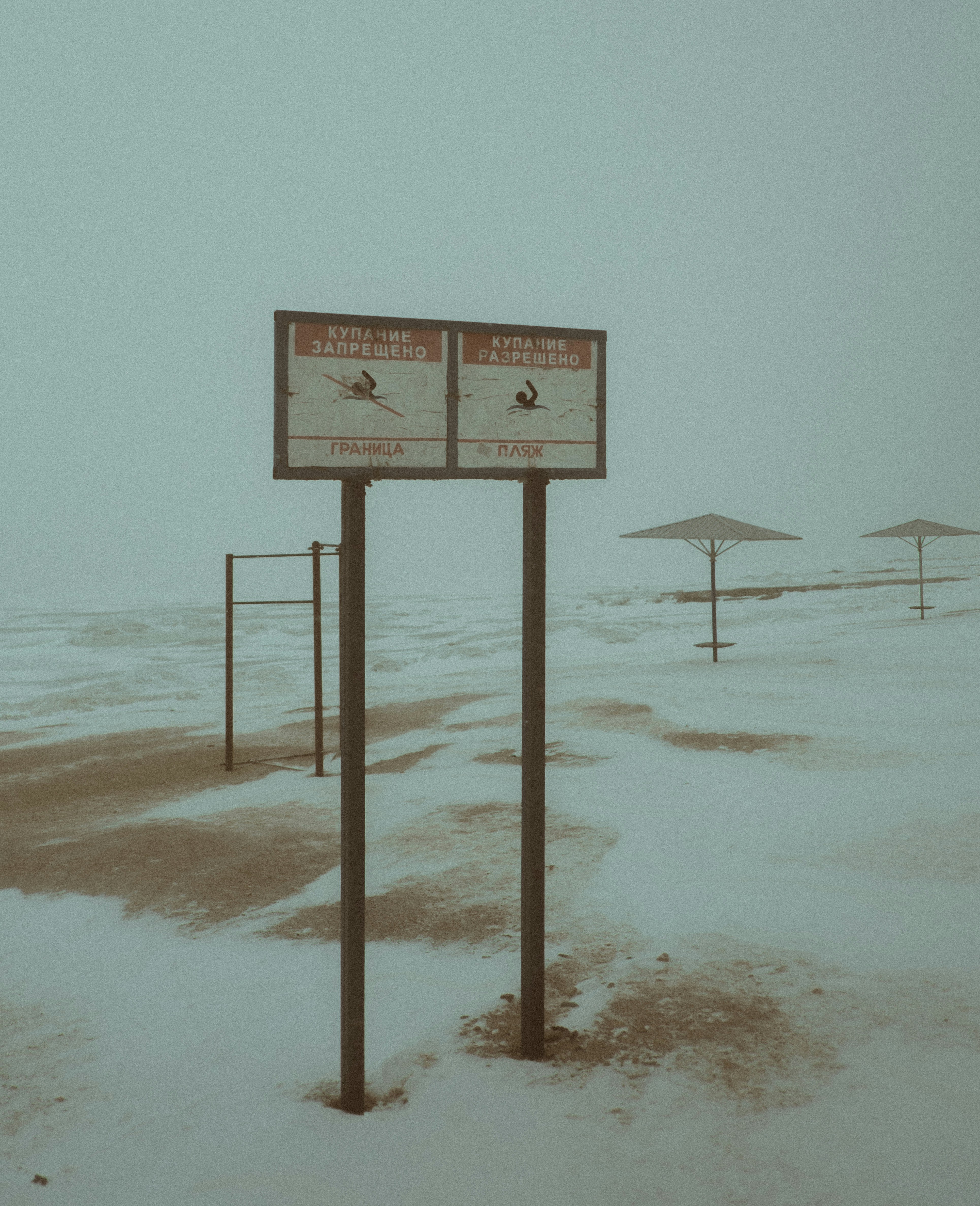 Two signs in a snowy landscape with beach umbrellas.
