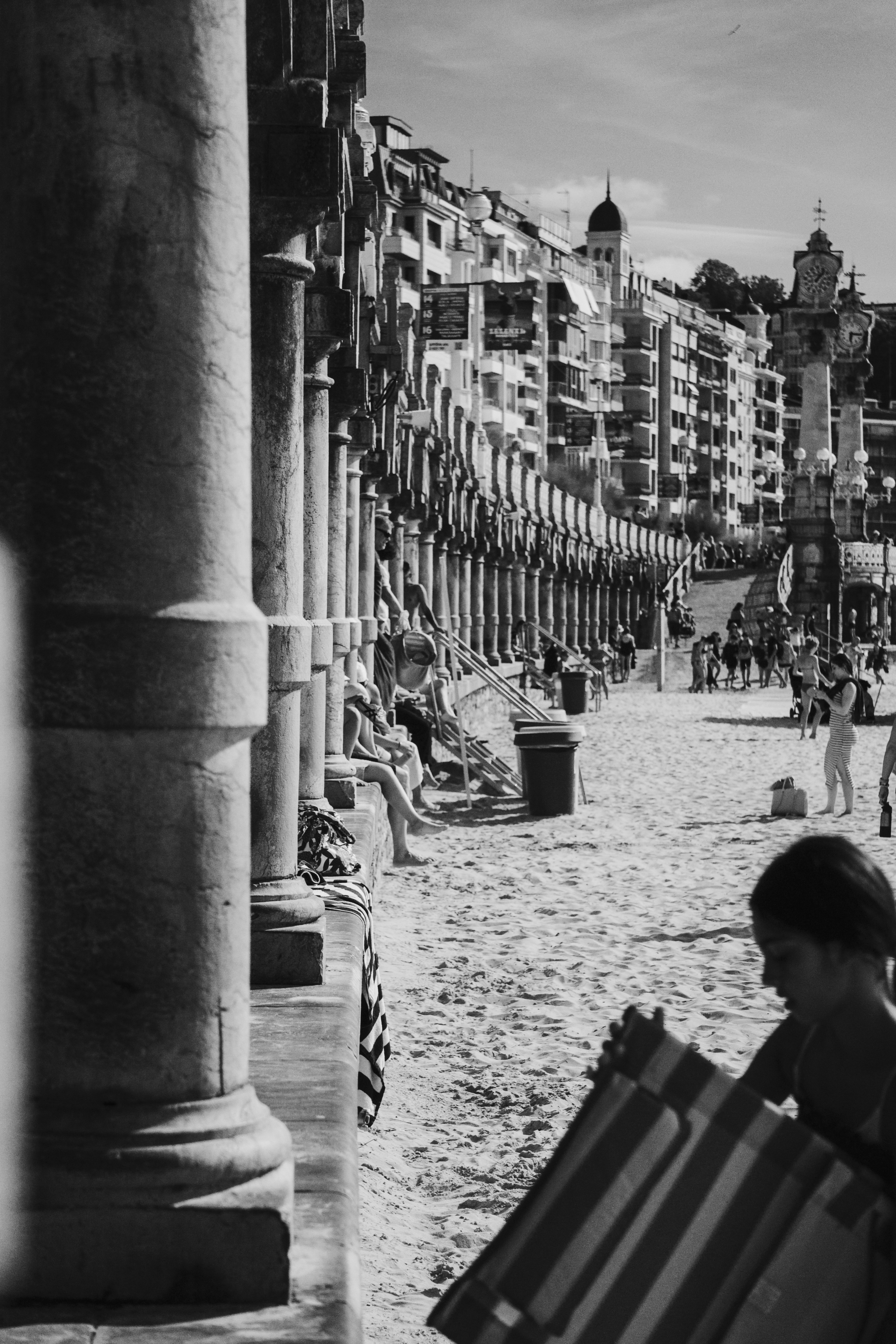 People relaxing on a sandy beach with buildings in background.
