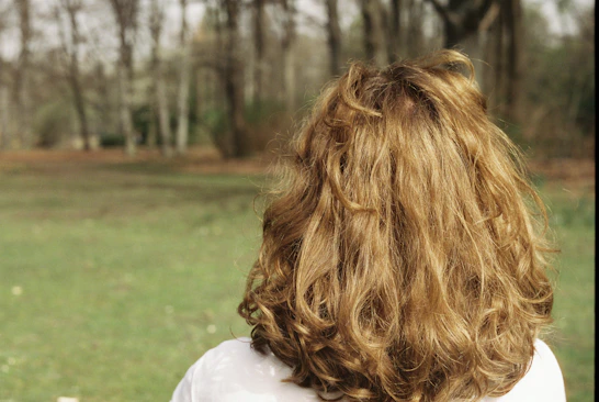 Woman with long curly blonde hair in a park.