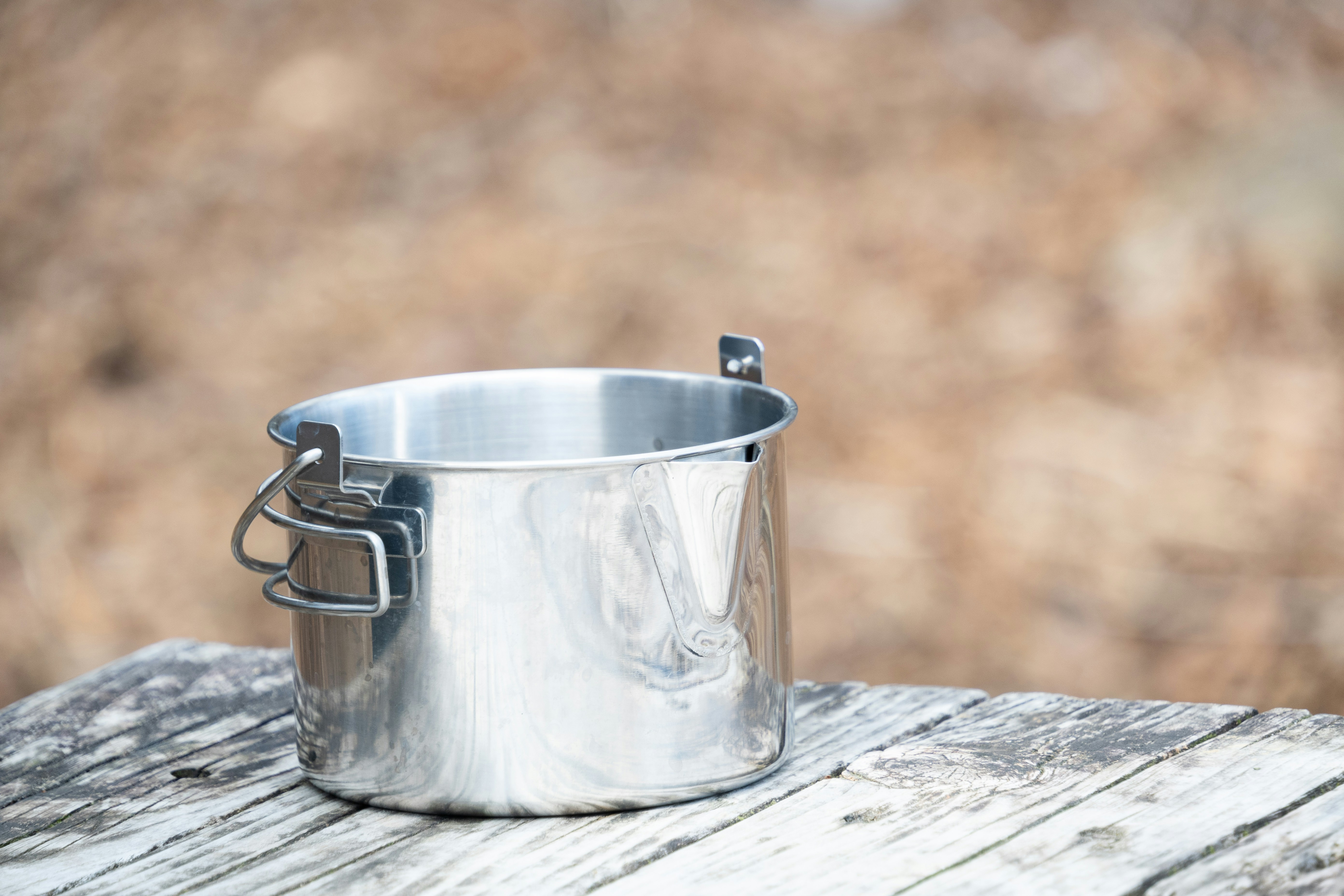 Ein glänzender Metalltopf mit Griff steht auf Holz.