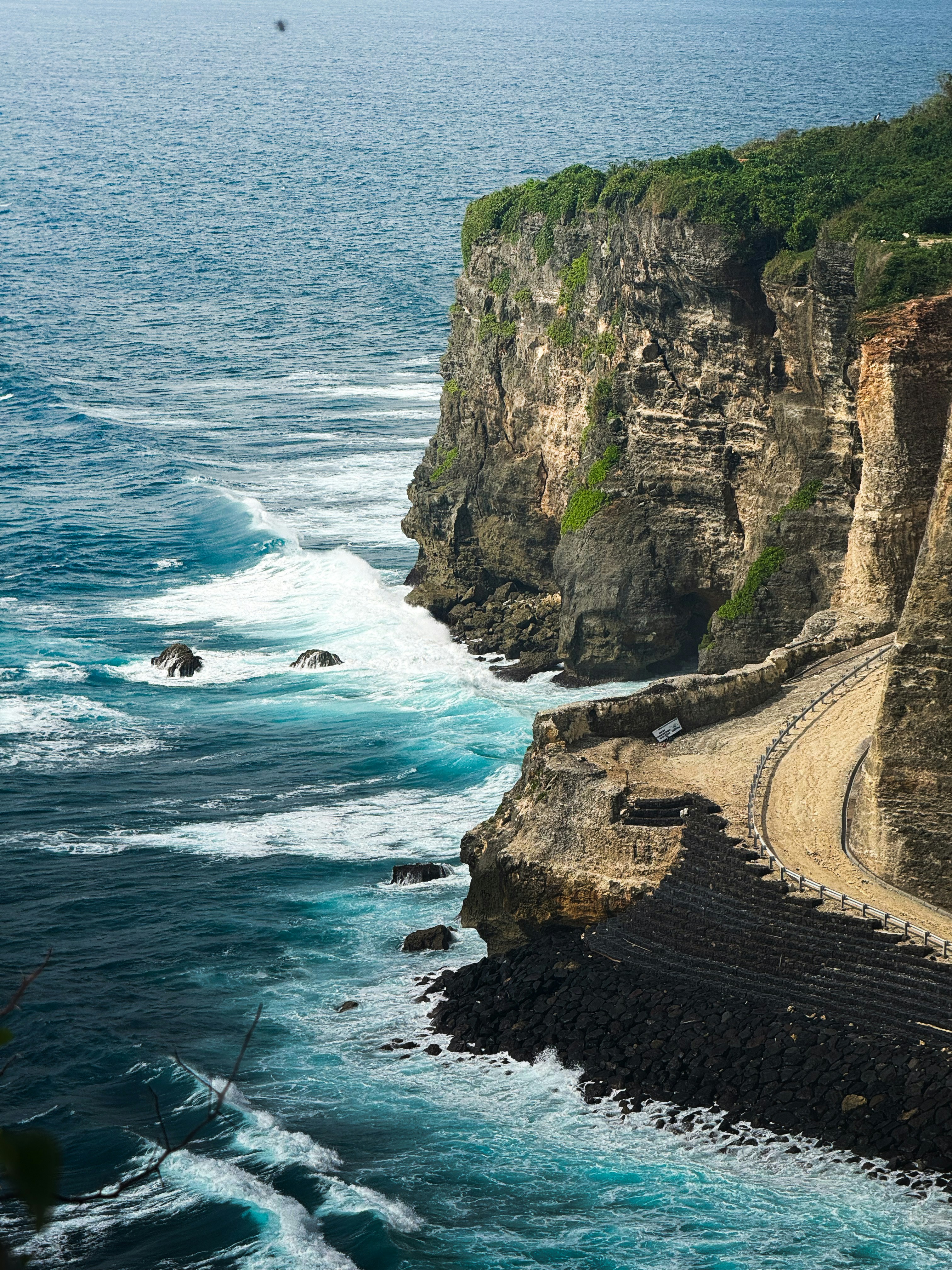 Rugged cliffs meet the turquoise ocean with crashing waves.