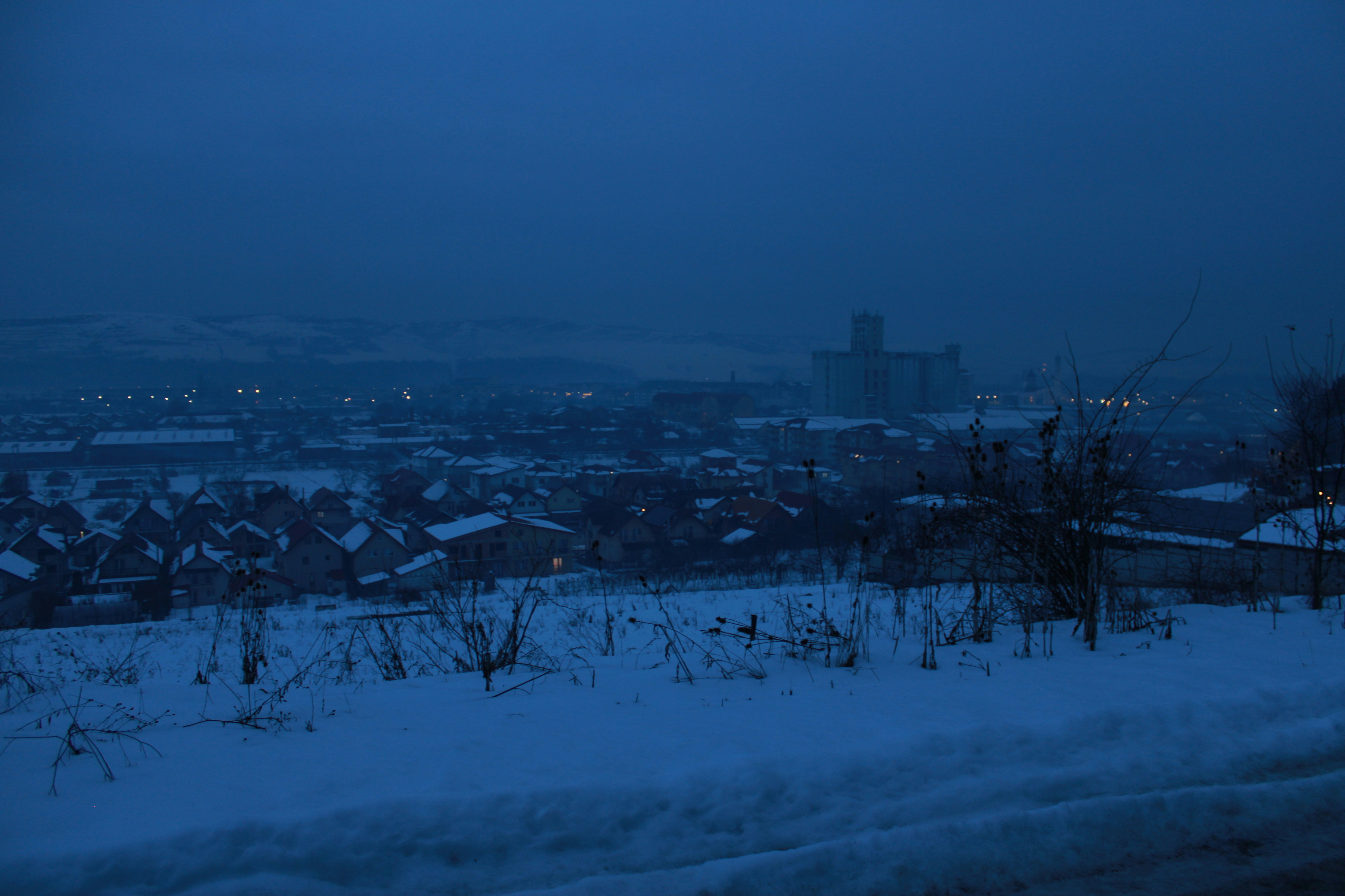 Snowy landscape with distant buildings at dusk