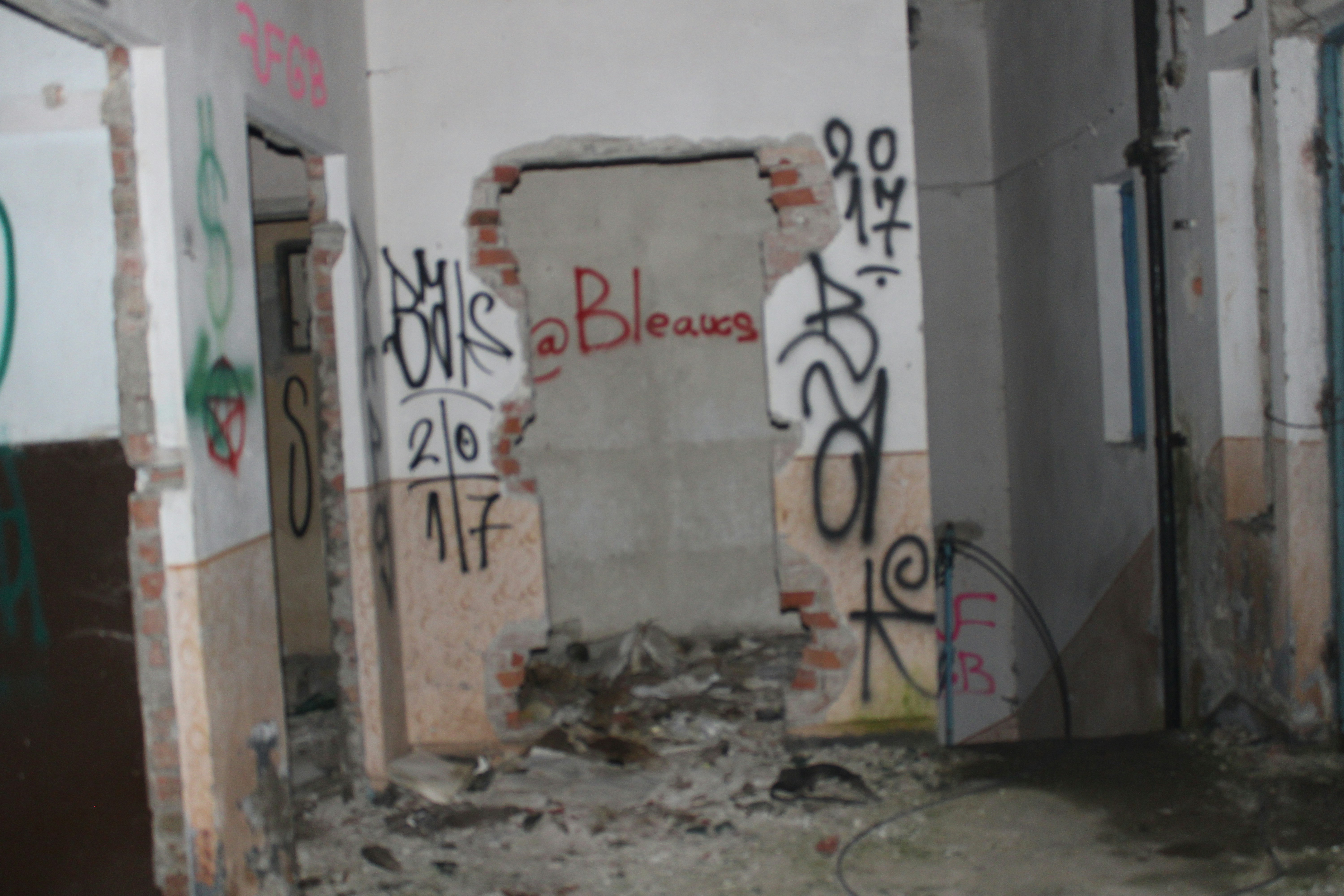 Graffiti covers a damaged interior wall with debris.