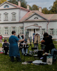 People painting outdoors in front of a large house