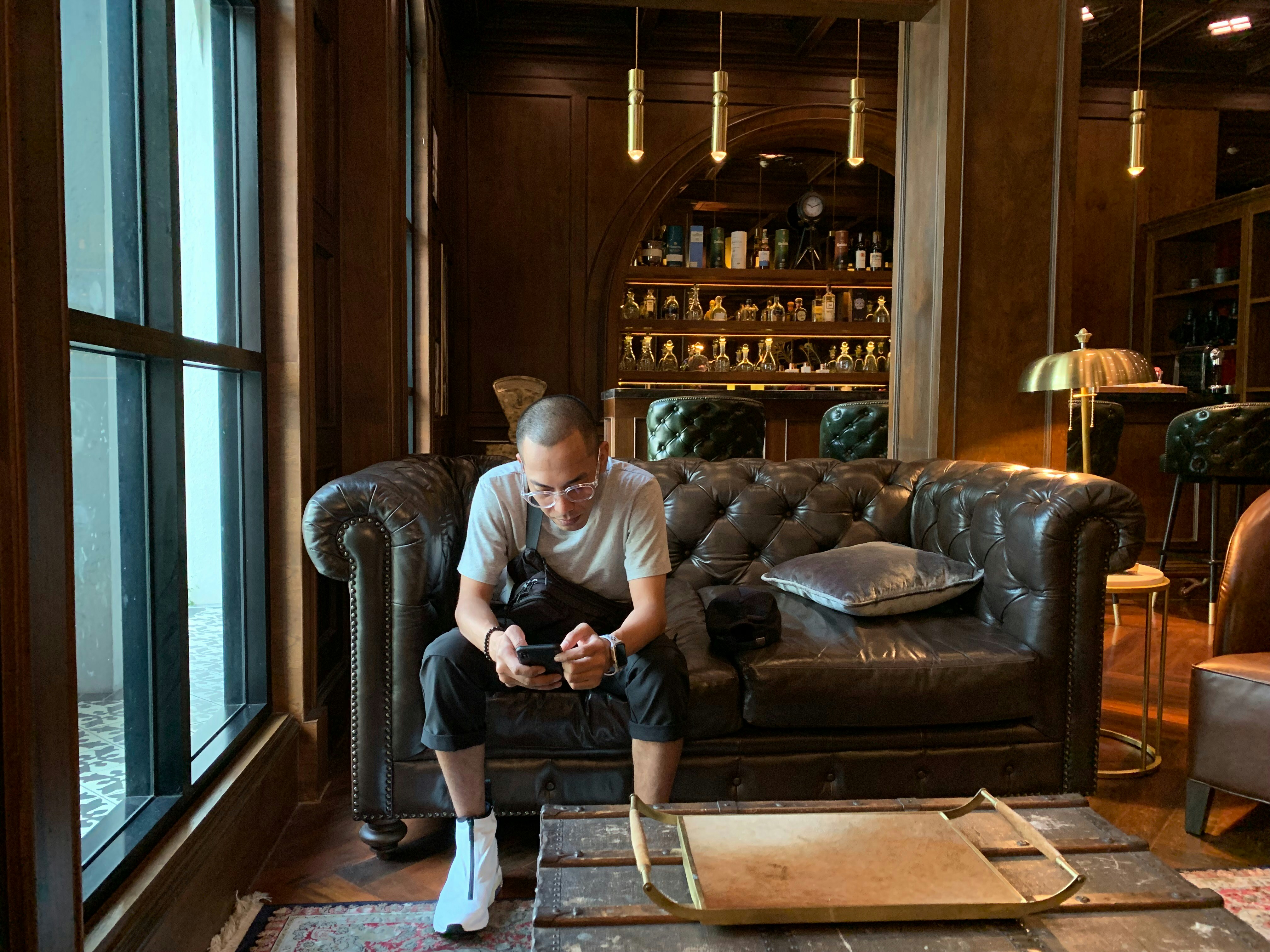 Man sitting on a leather couch looking at phone.