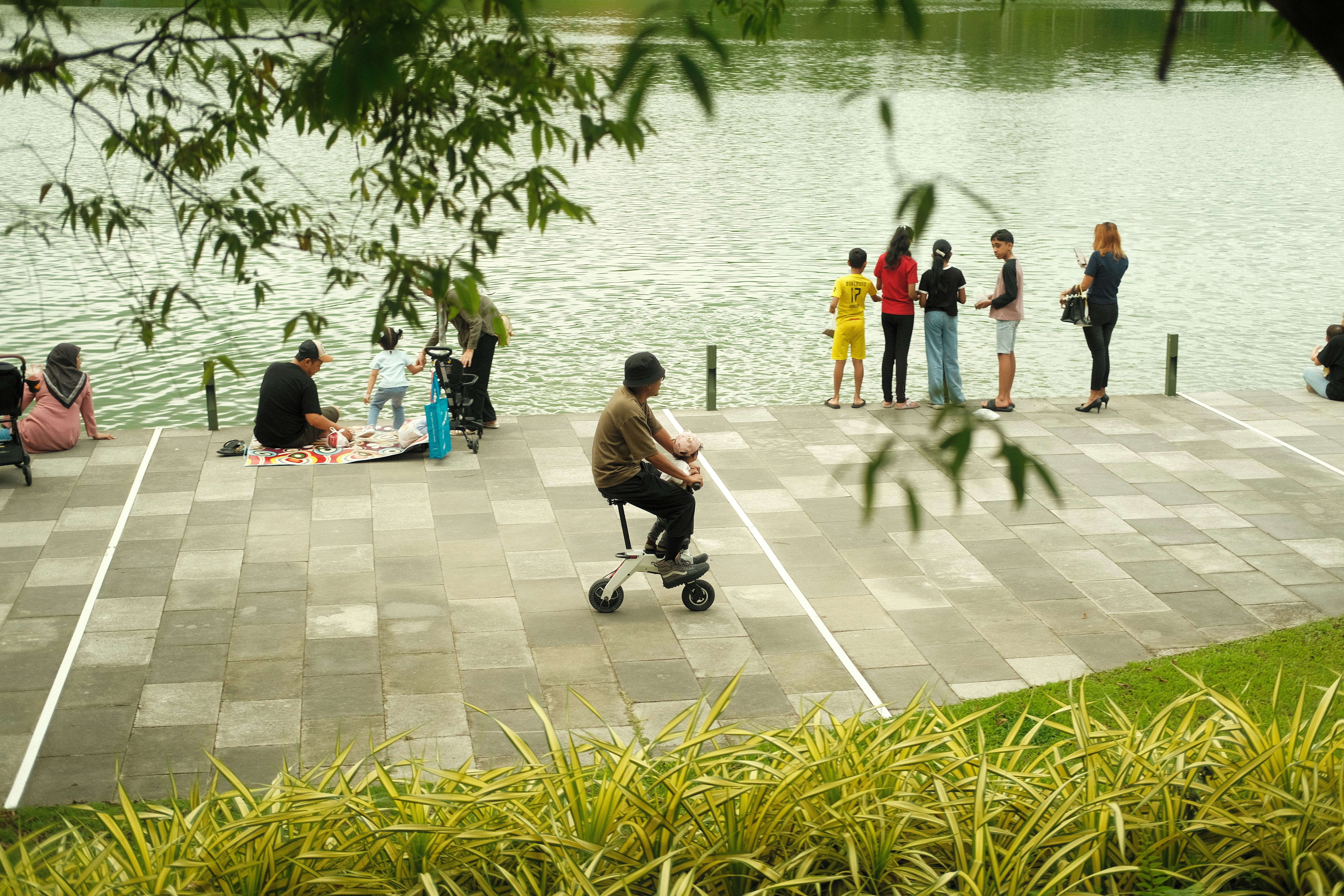 People gather by a lake, one rides a scooter.
