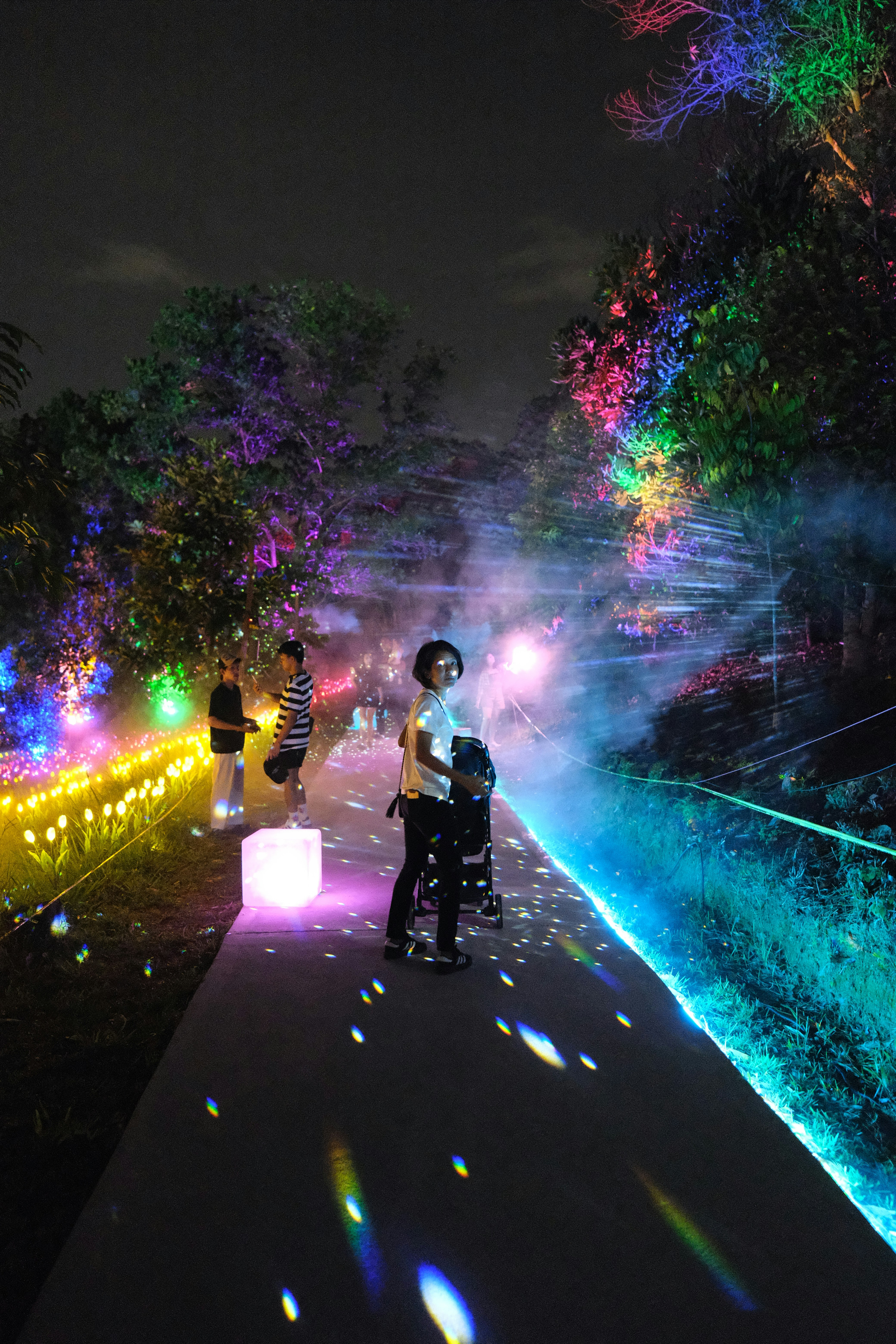 People walk through a colorful light display at night.