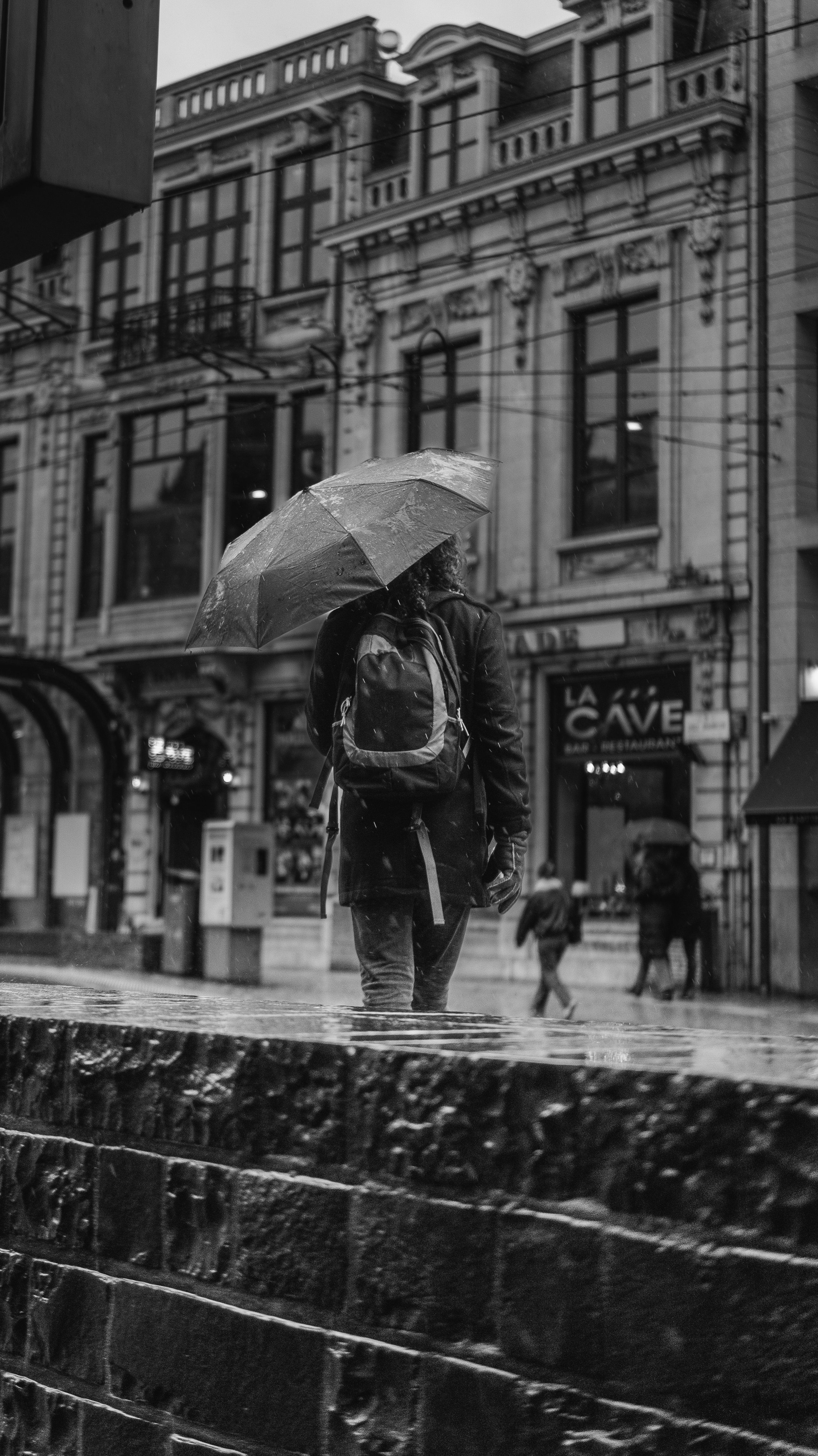Person with umbrella walks in the rain on city street.