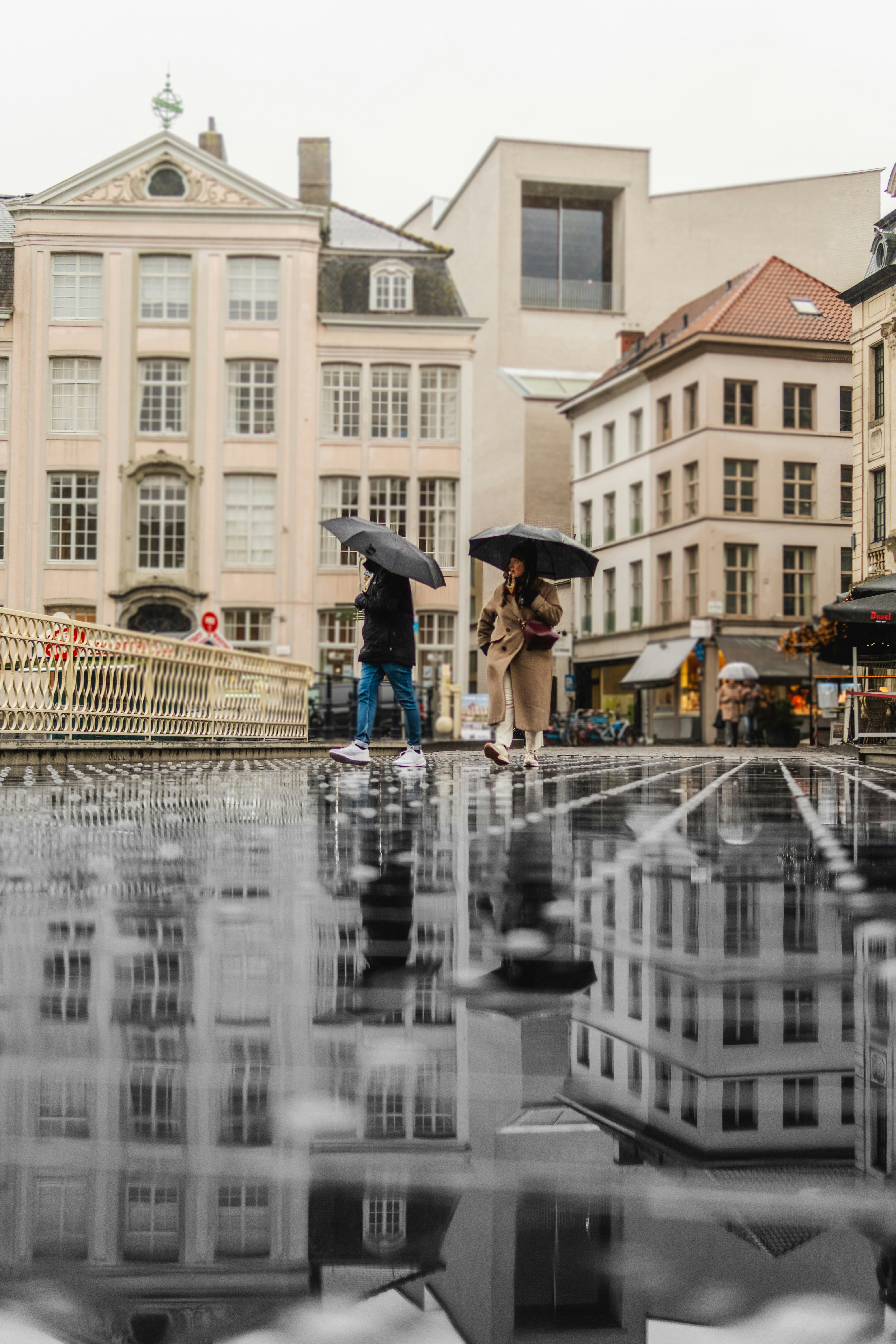 Two people with umbrellas walk on wet city street