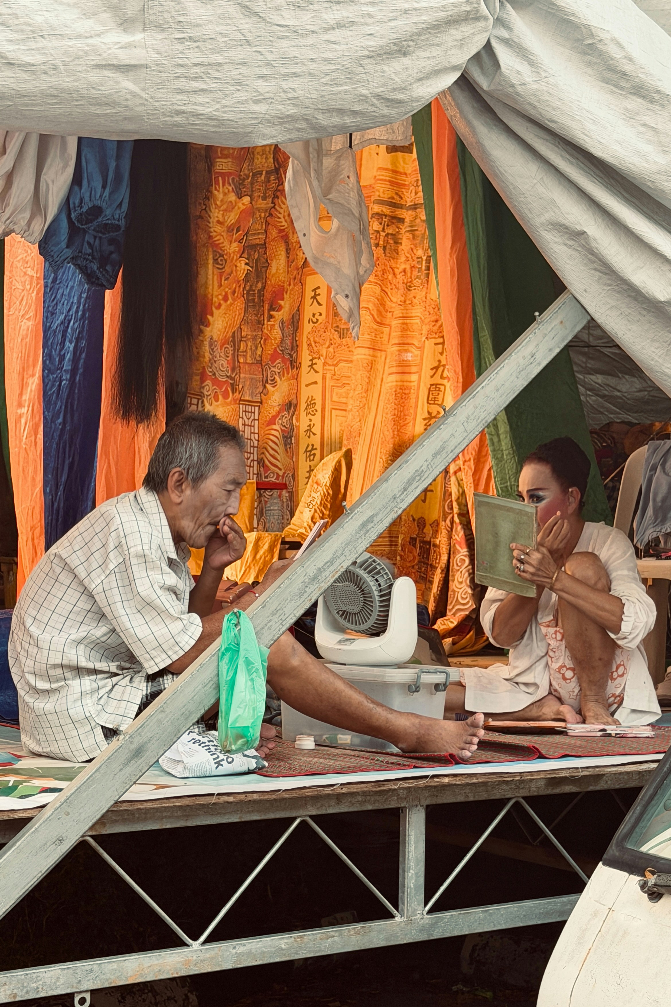 Man and woman applying makeup under a tent.