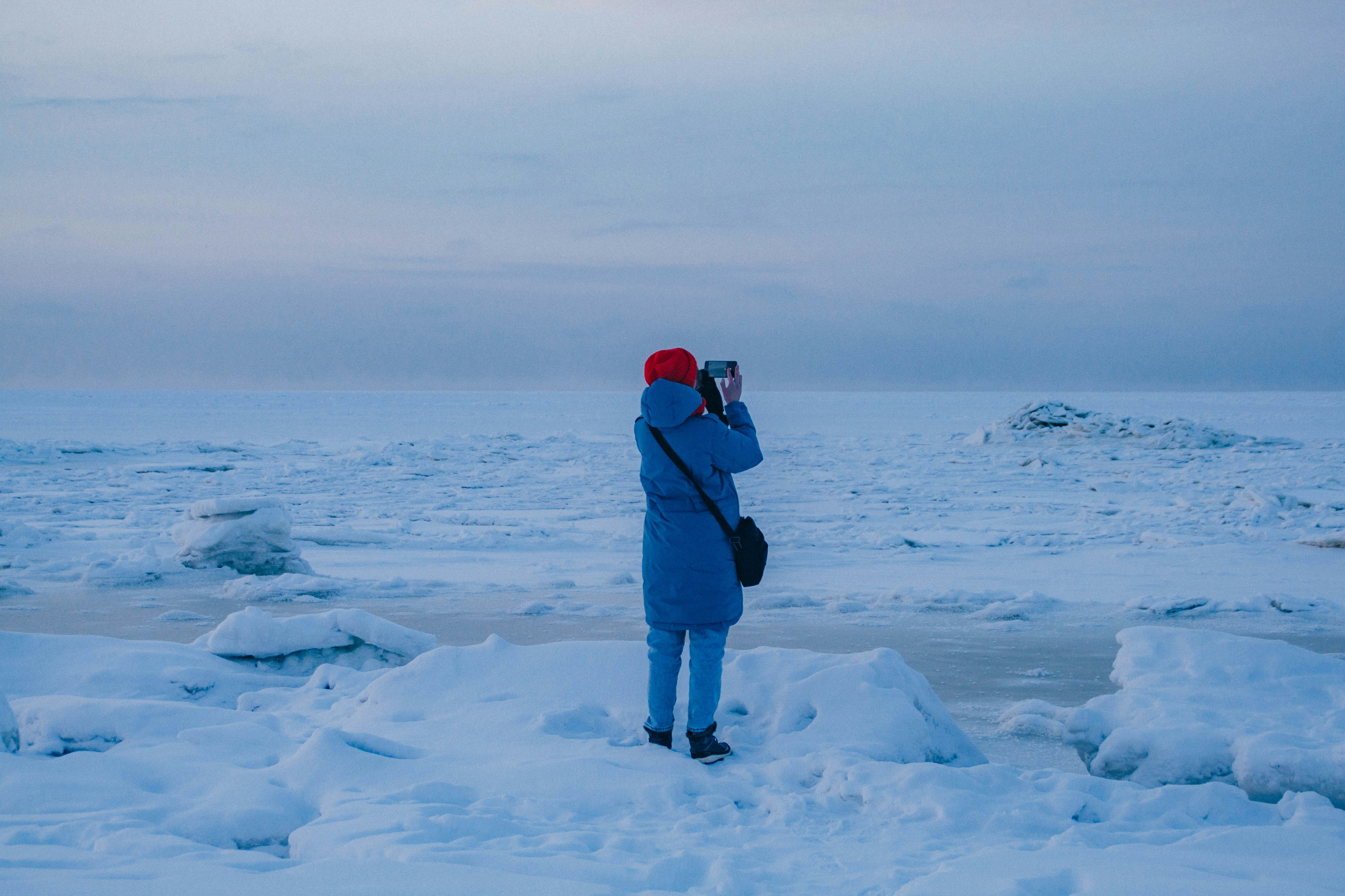 Person in blue coat photographs icy landscape at dusk