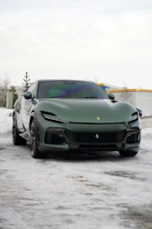 A green ferrari parked on a snowy road.