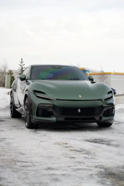 A green ferrari parked on a snowy road.
