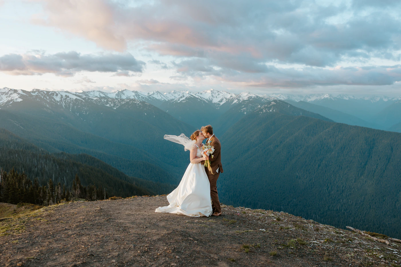 A bride and groom sharing an intimate moment during their mountain elopement wedding with warm morning light illuminating them and dramatic mountain peaks and wilderness landscape behind them