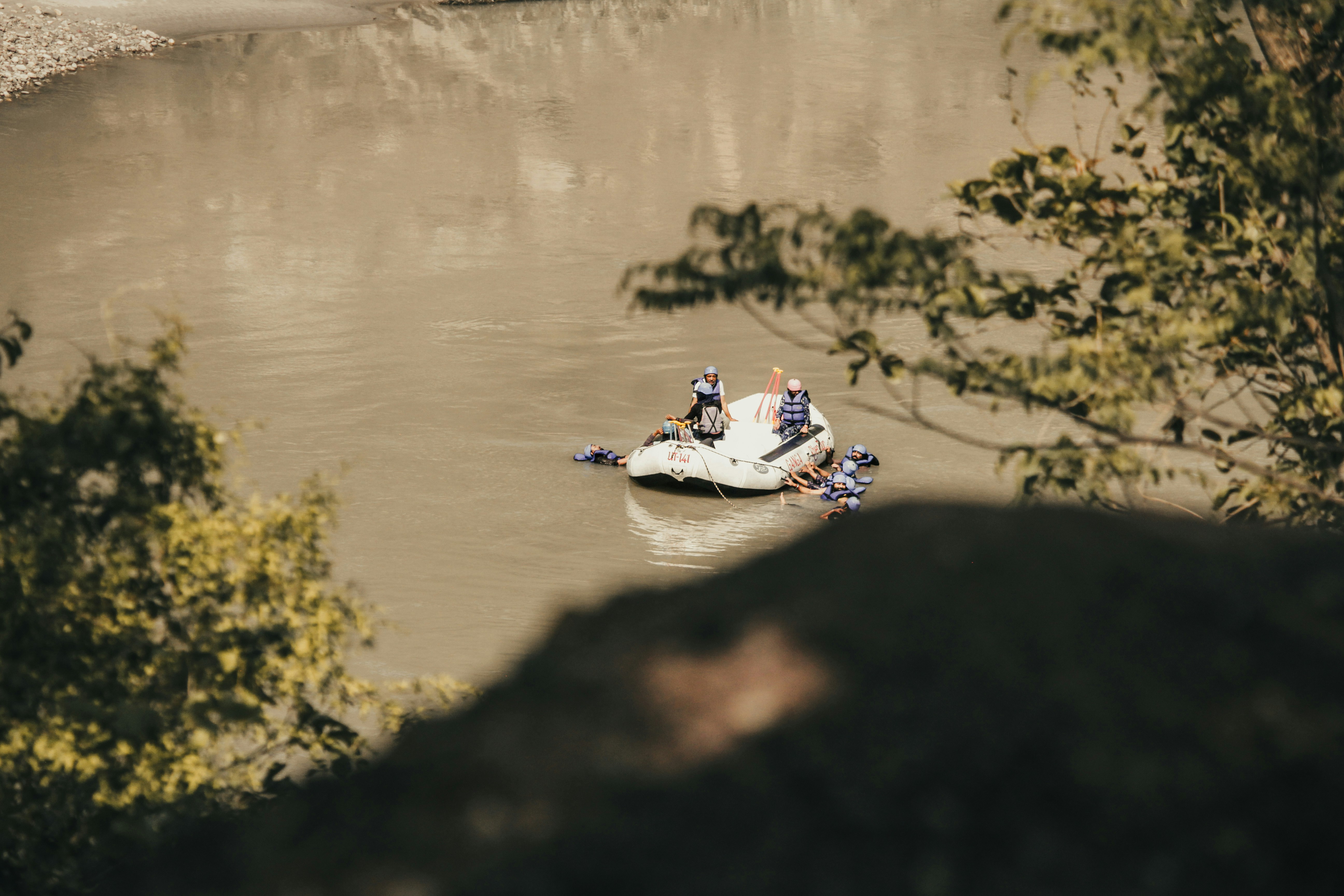 People raft down a muddy river surrounded by trees