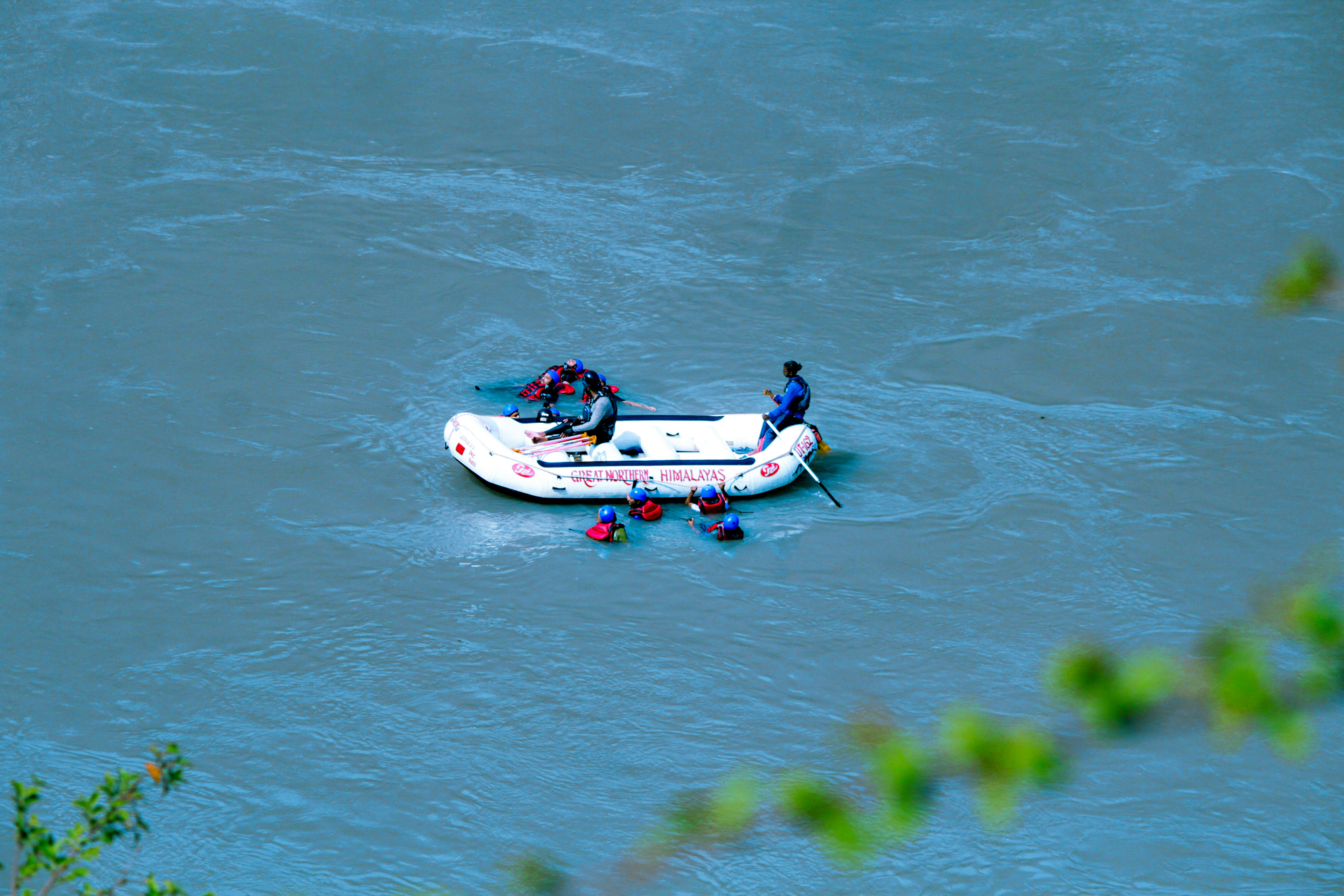 A capsized boat partially submerged in a river, with rescue workers in smaller boats nearby and debris floating.