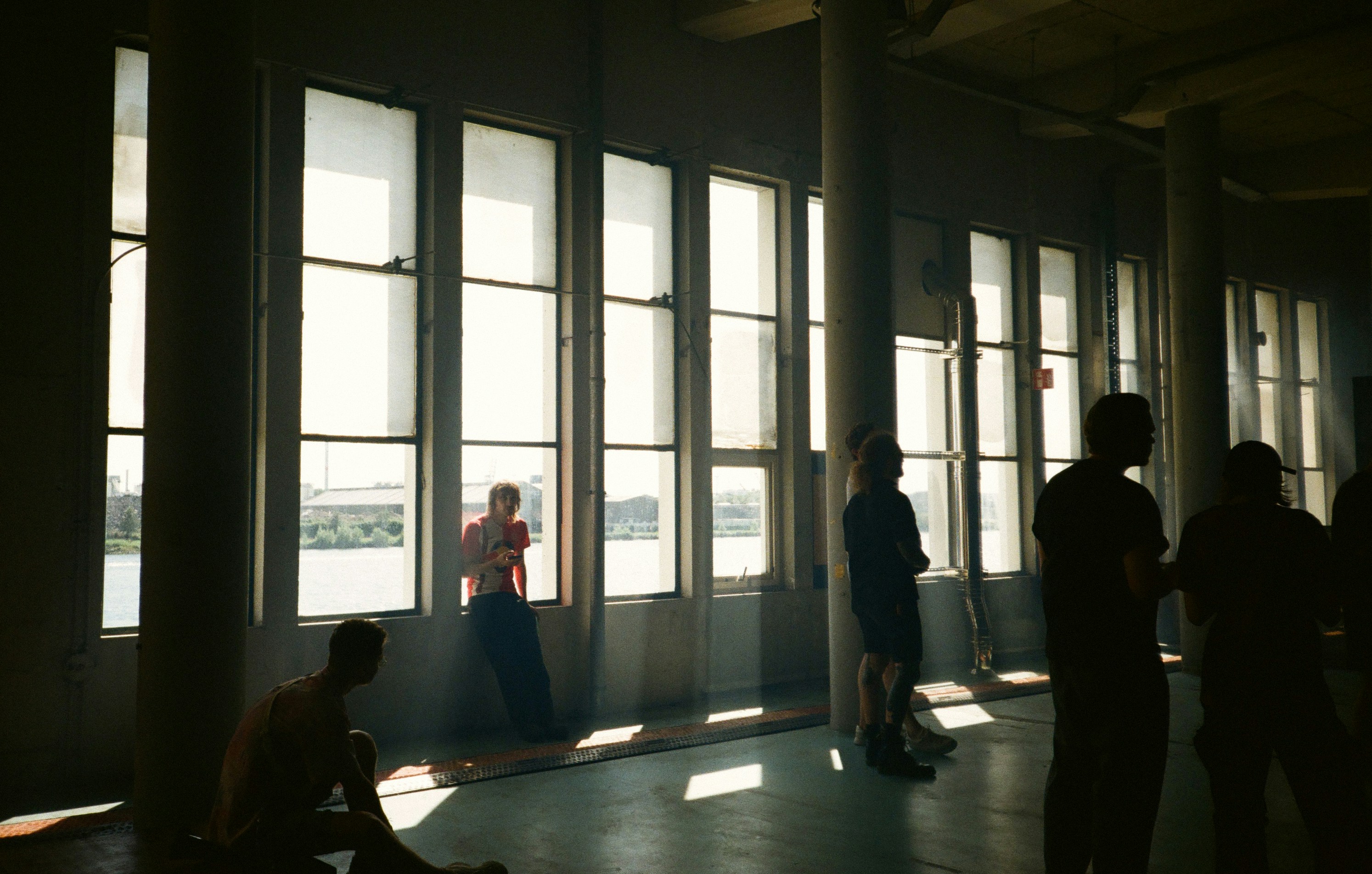 Le persone si stagliano contro grandi finestre con la luce del sole che filtra.