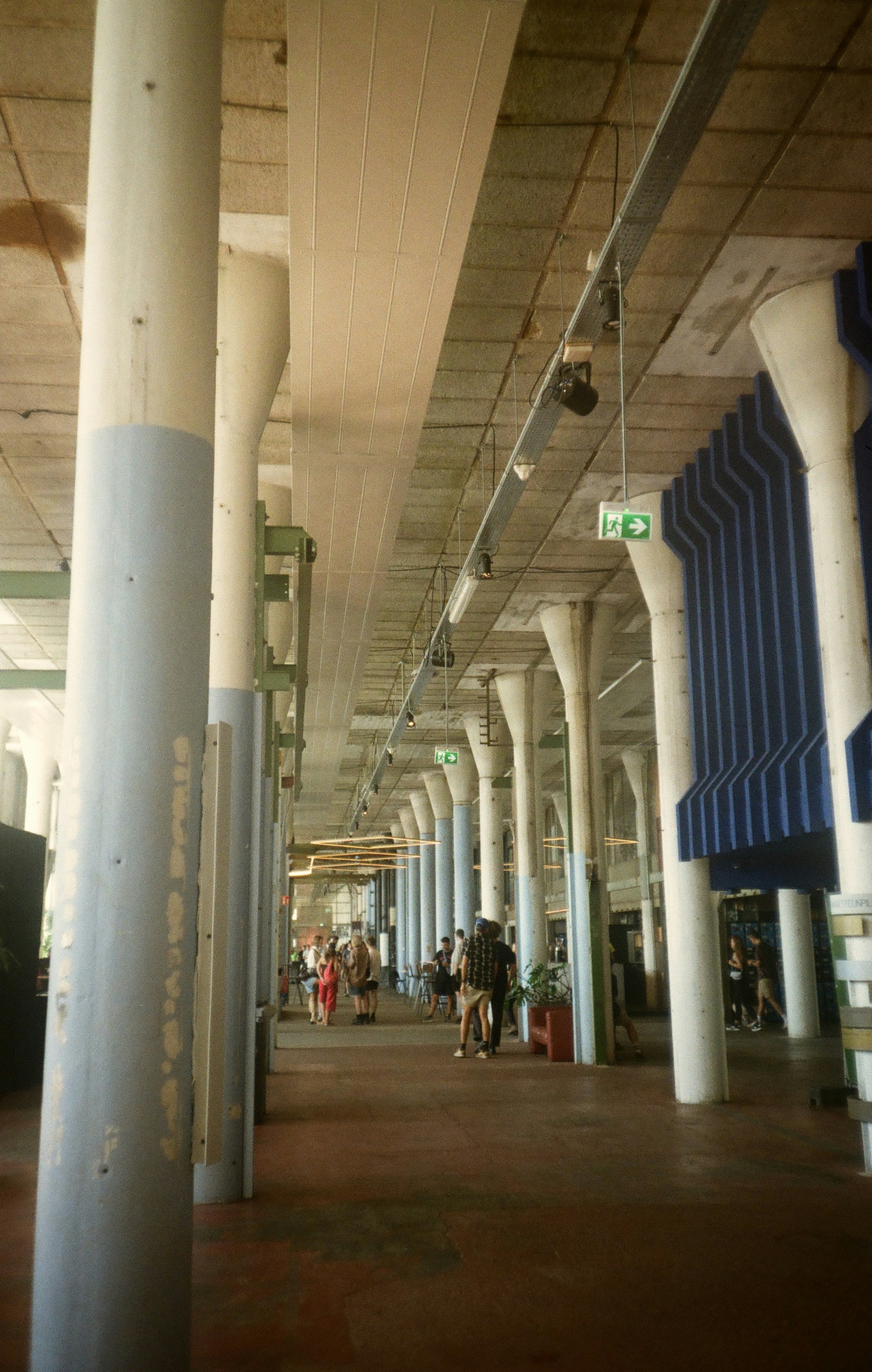 Persone che camminano lungo un lungo vialetto interno fiancheggiato da pilastri.