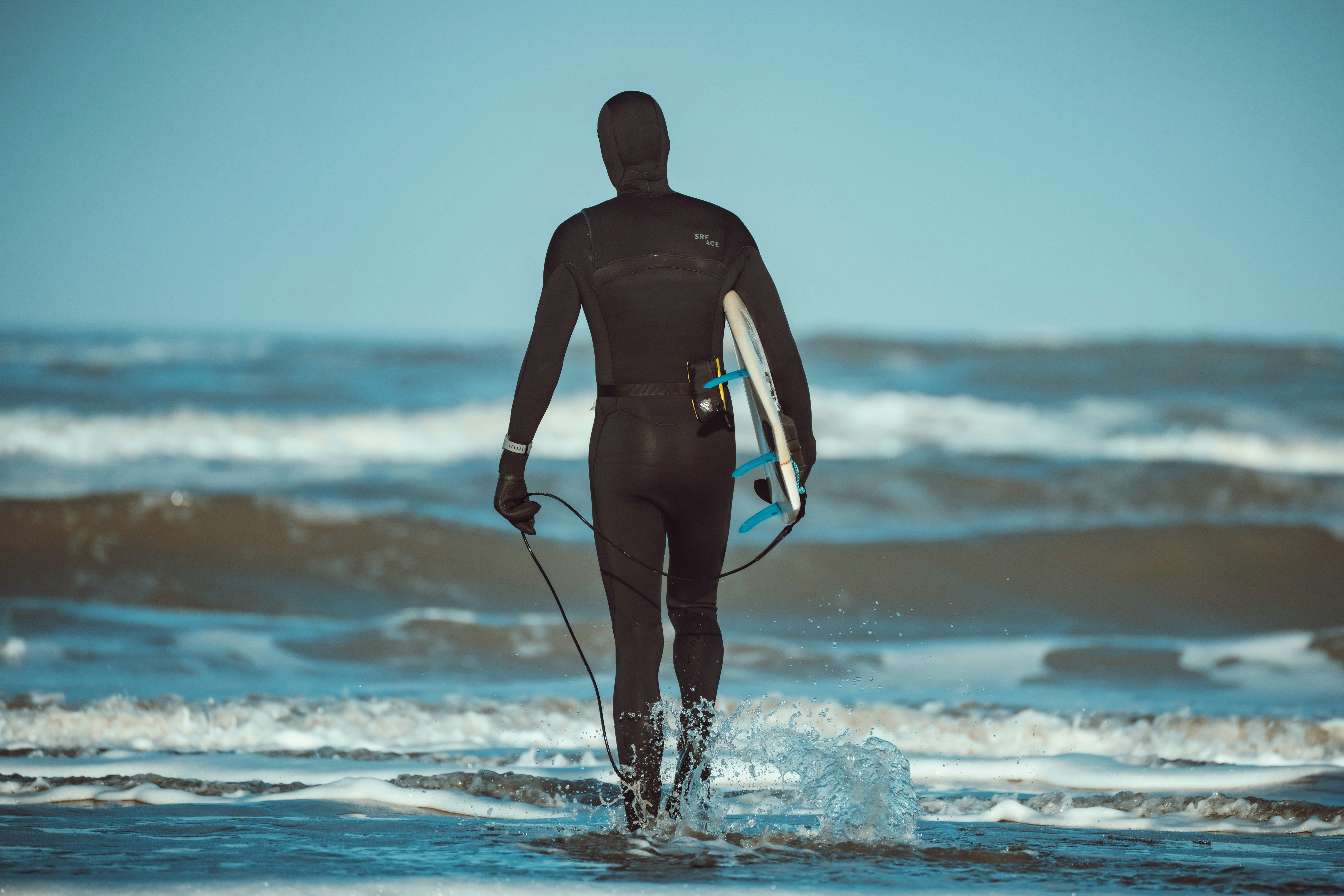 웻수트를 입은 서퍼가 서핑보드를 들고 바다로 걸어 들어갑니다