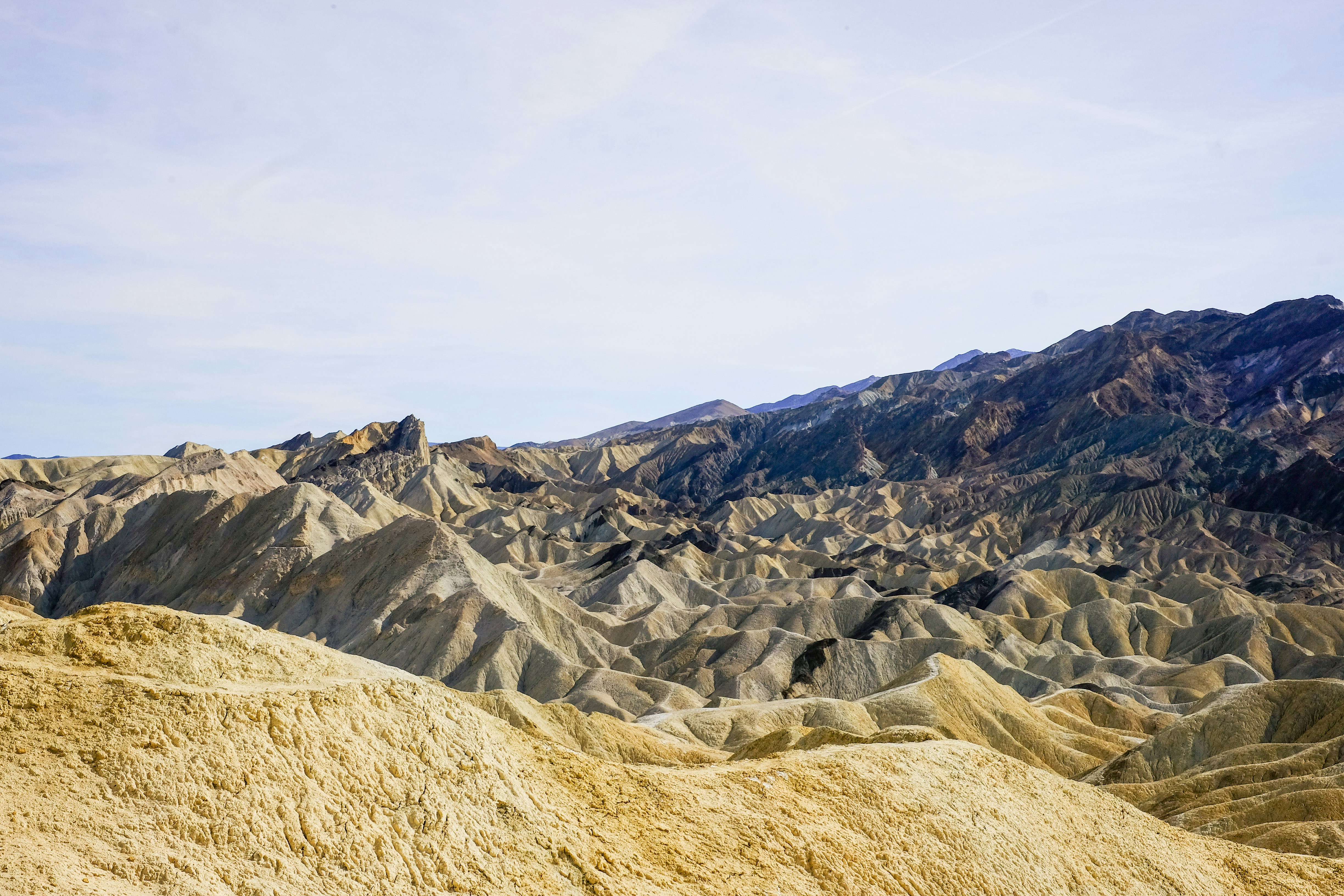 澄んだ空の下、重なった丘が広がる険しい砂漠の風景