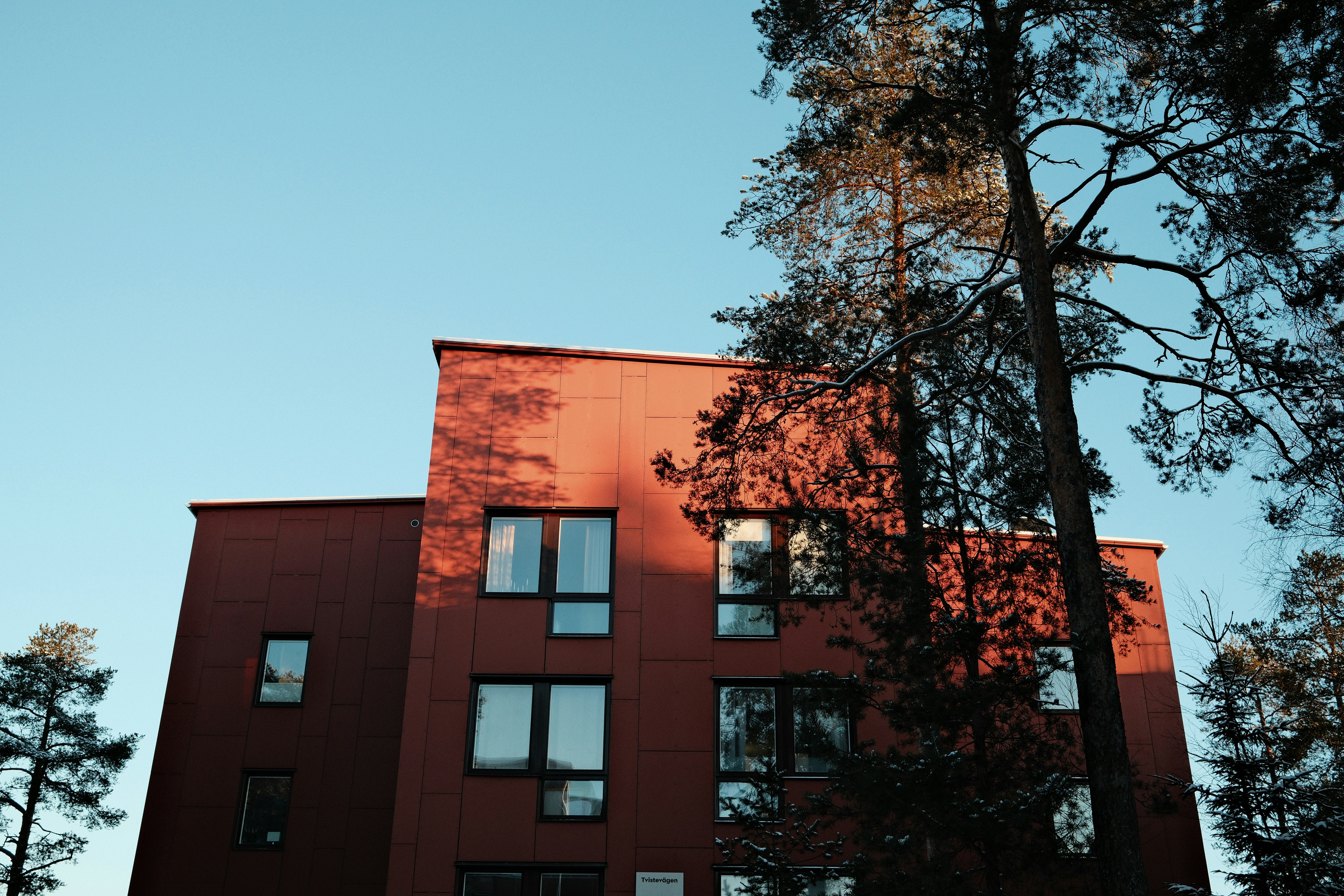 Modern red building with trees against blue sky.