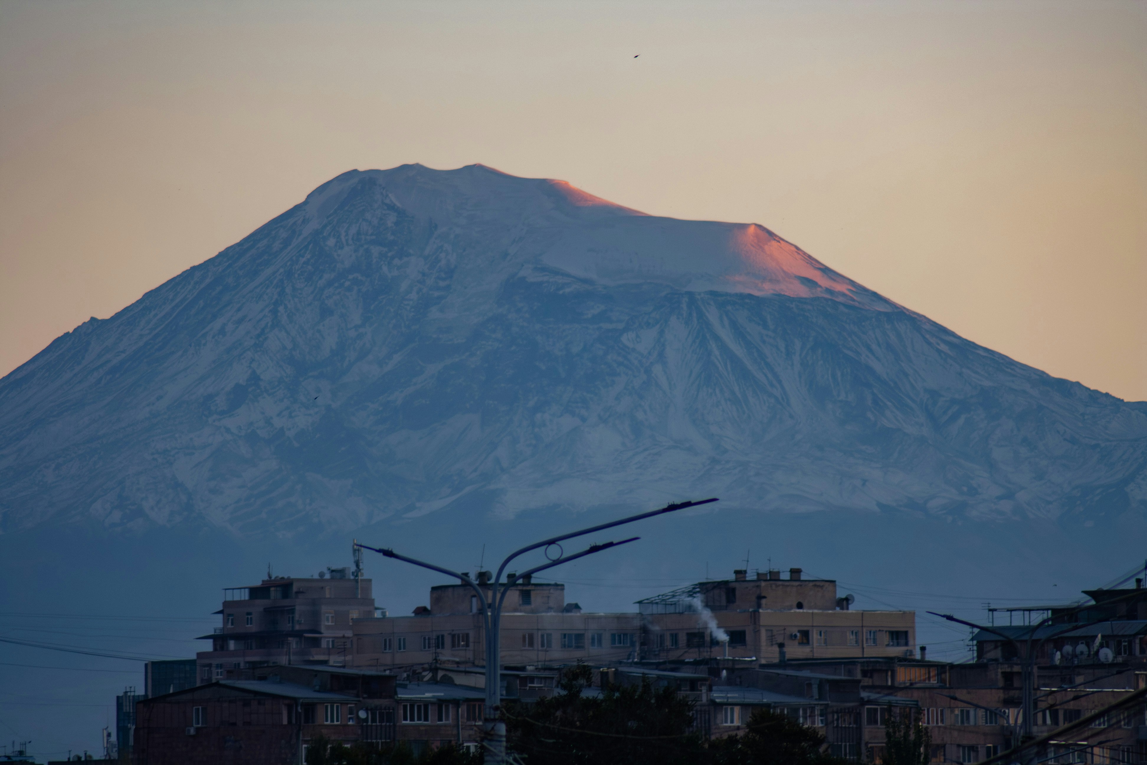 Snow-capped mountain peak at sunset over buildings