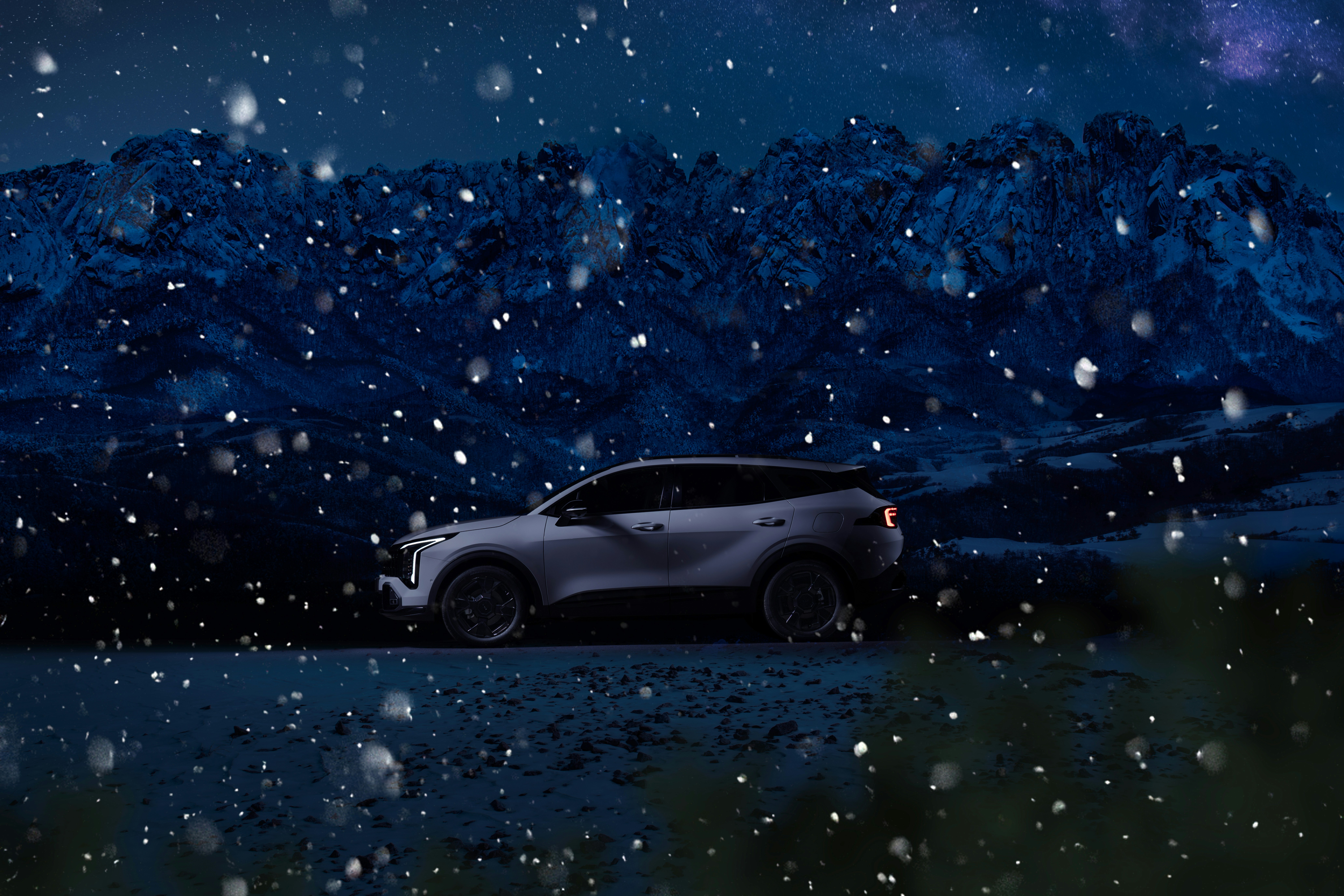 A car parked on a snowy mountain road at night.